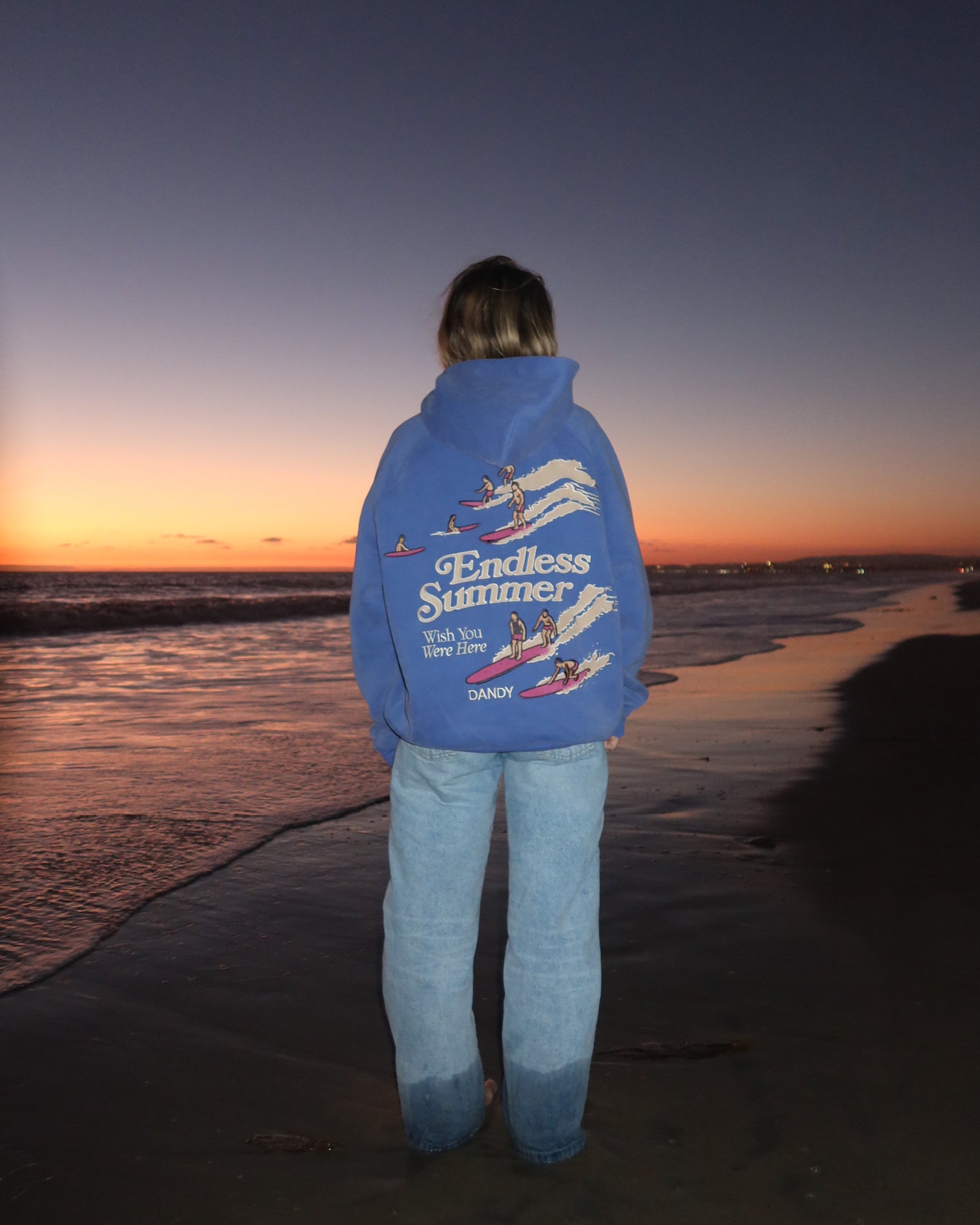 "Endless Summer" Oversized Lux Hoodie in Vintage Washed Blue standing on the beach at sunset
