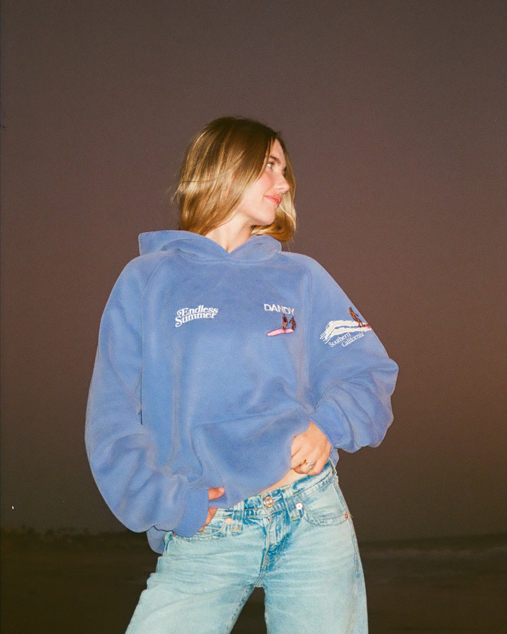 "Endless Summer" Oversized Lux Hoodie in Vintage Washed Blue showing the front of the hoodie on the beach at sunset