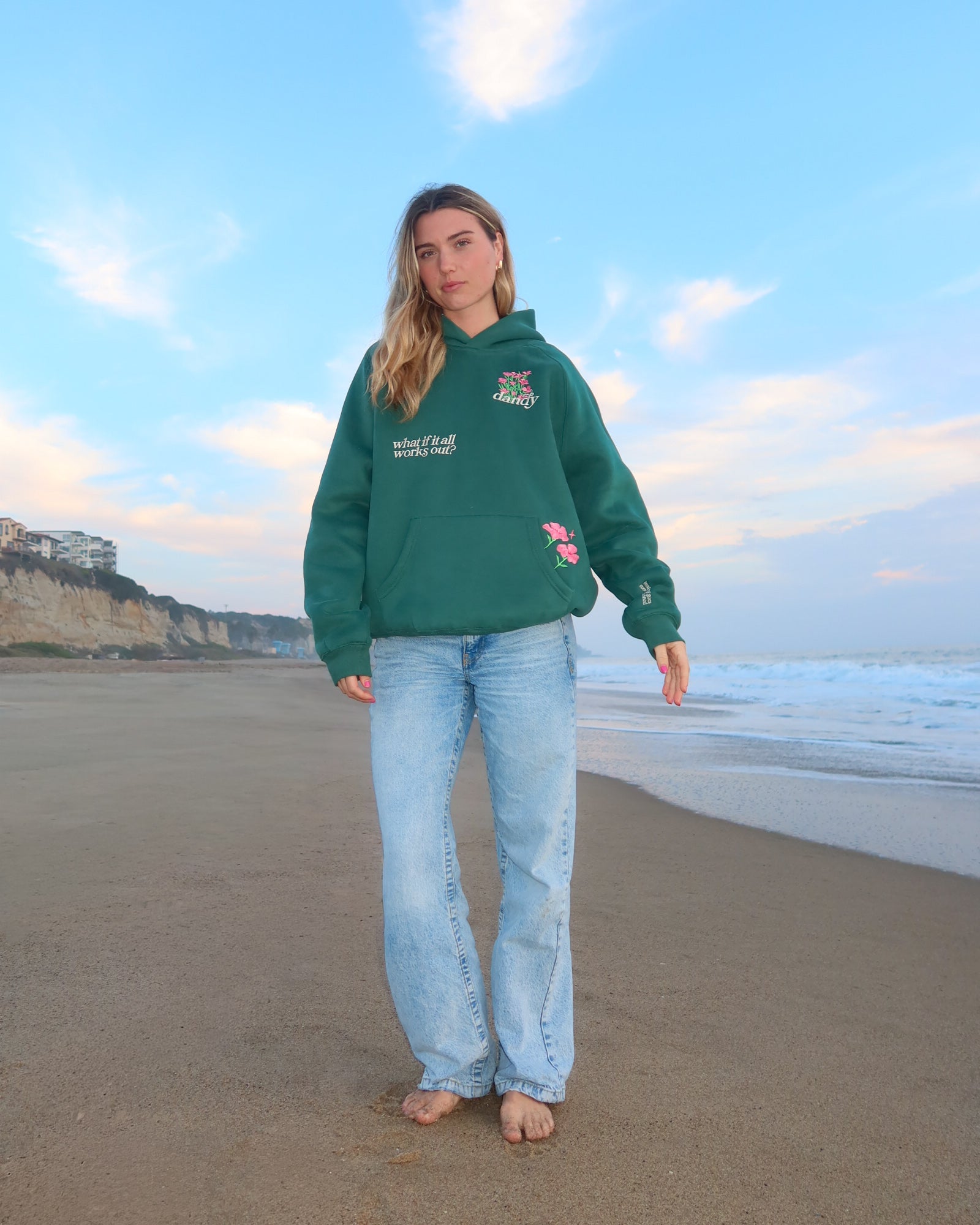 Person wearing a green hoodie with a logo on a beach