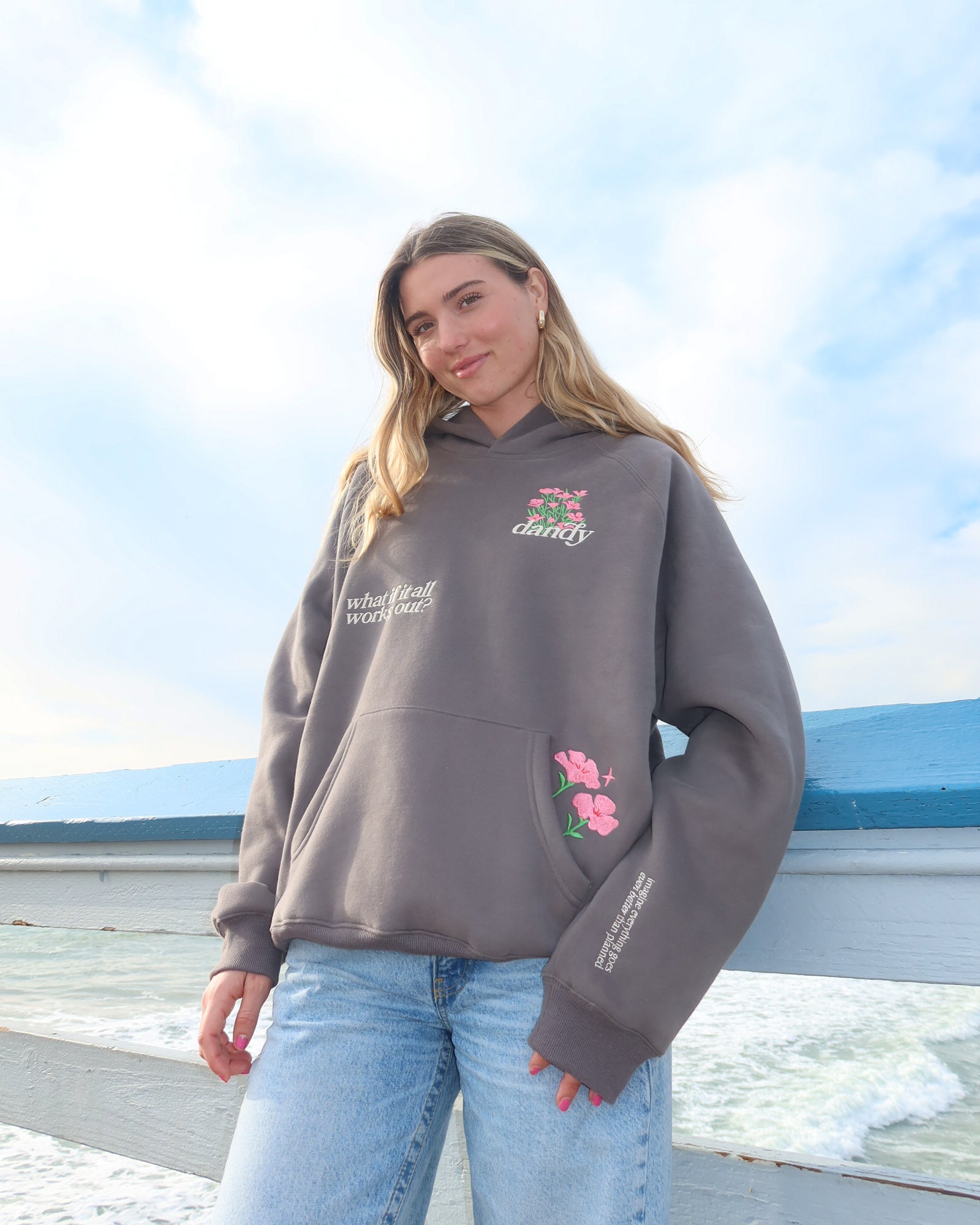 Person wearing a gray hoodie with floral designs on a beach