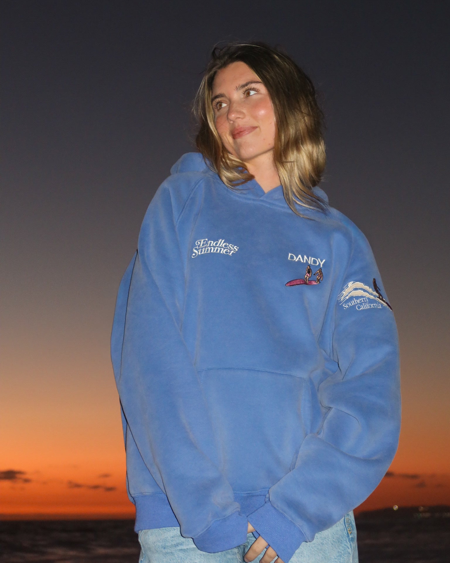"Endless Summer" Oversized Lux Hoodie in Vintage Washed Blue showing the front of the hoodie on the beach at sunset