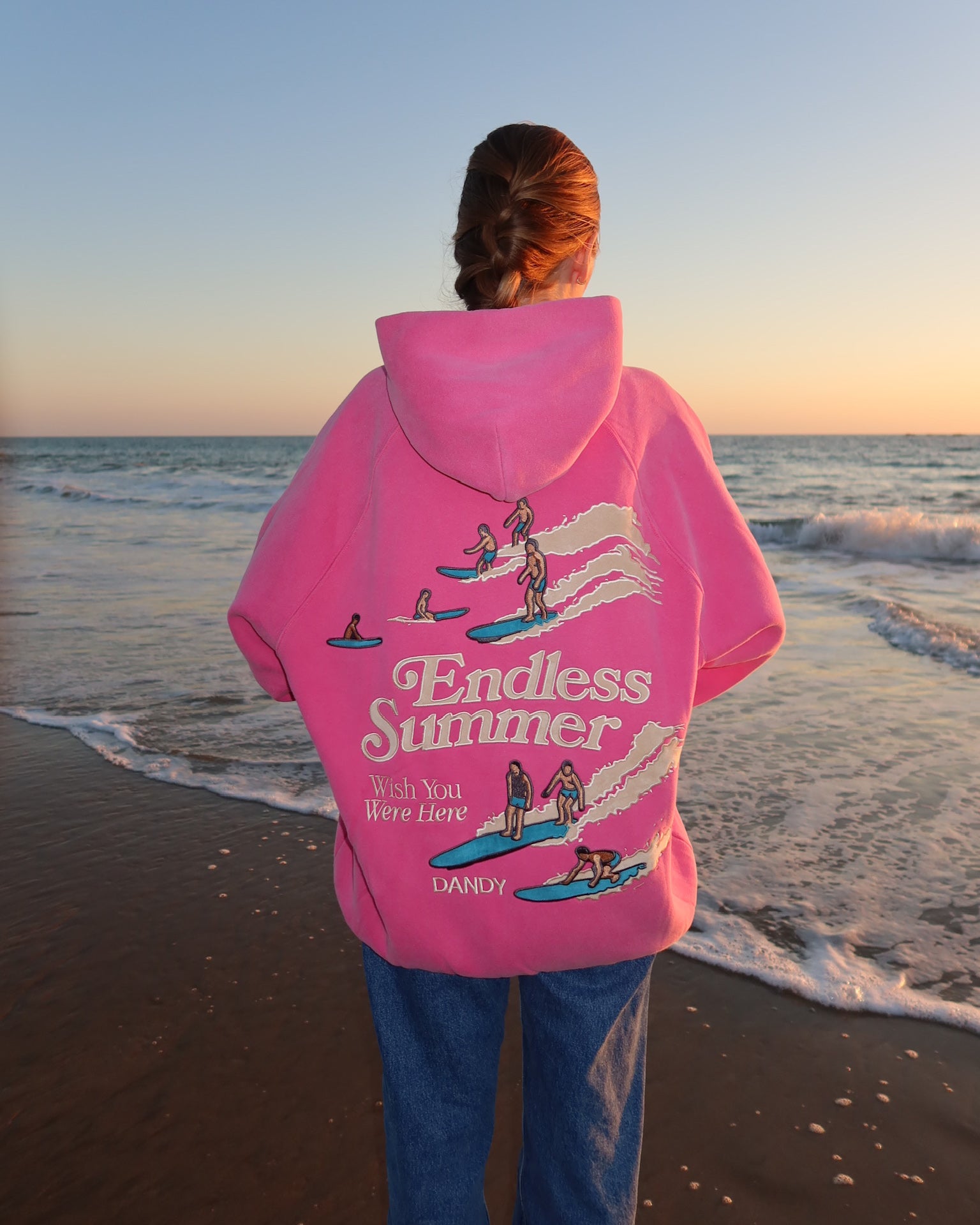 "Endless Summer" Oversized Lux Hoodie in Vintage Washed Pink on the beach at sunset with the ocean in the background
