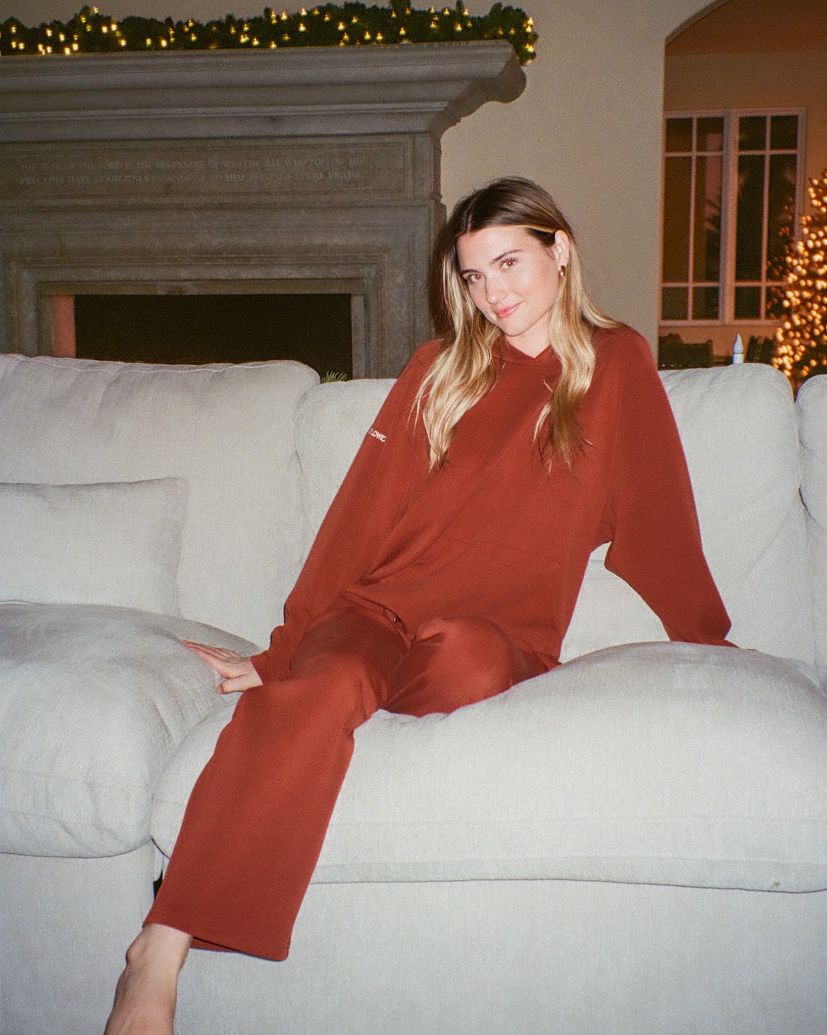 Woman in a red outfit sitting on a white couch in a cozy living room.