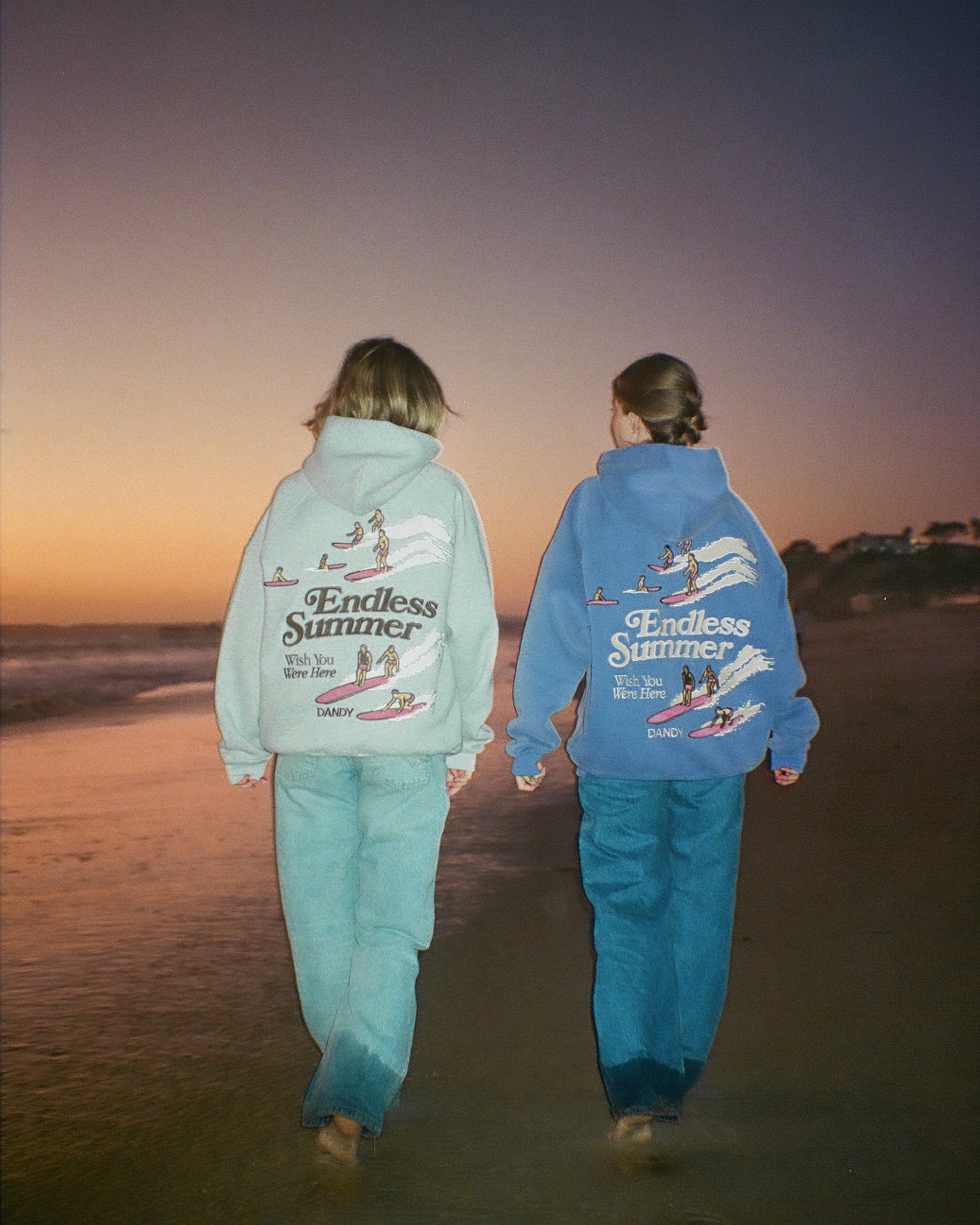 "Endless Summer" Oversized Lux Hoodie in Vintage Washed Blue standing next to the gray version of the hoodie on the beach