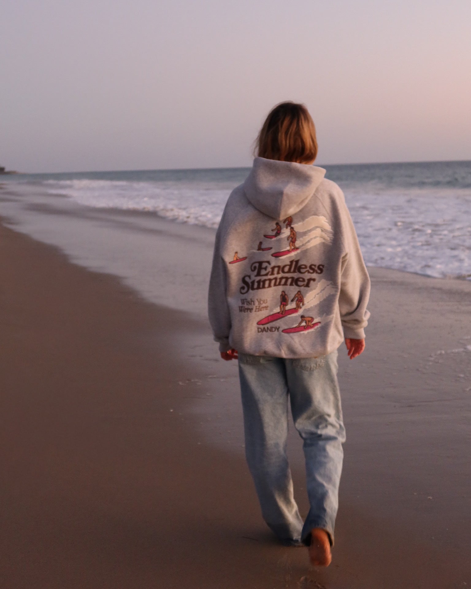 "Endless Summer" Oversized Lux Hoodie in Dark Heather walking on the beach at sunset