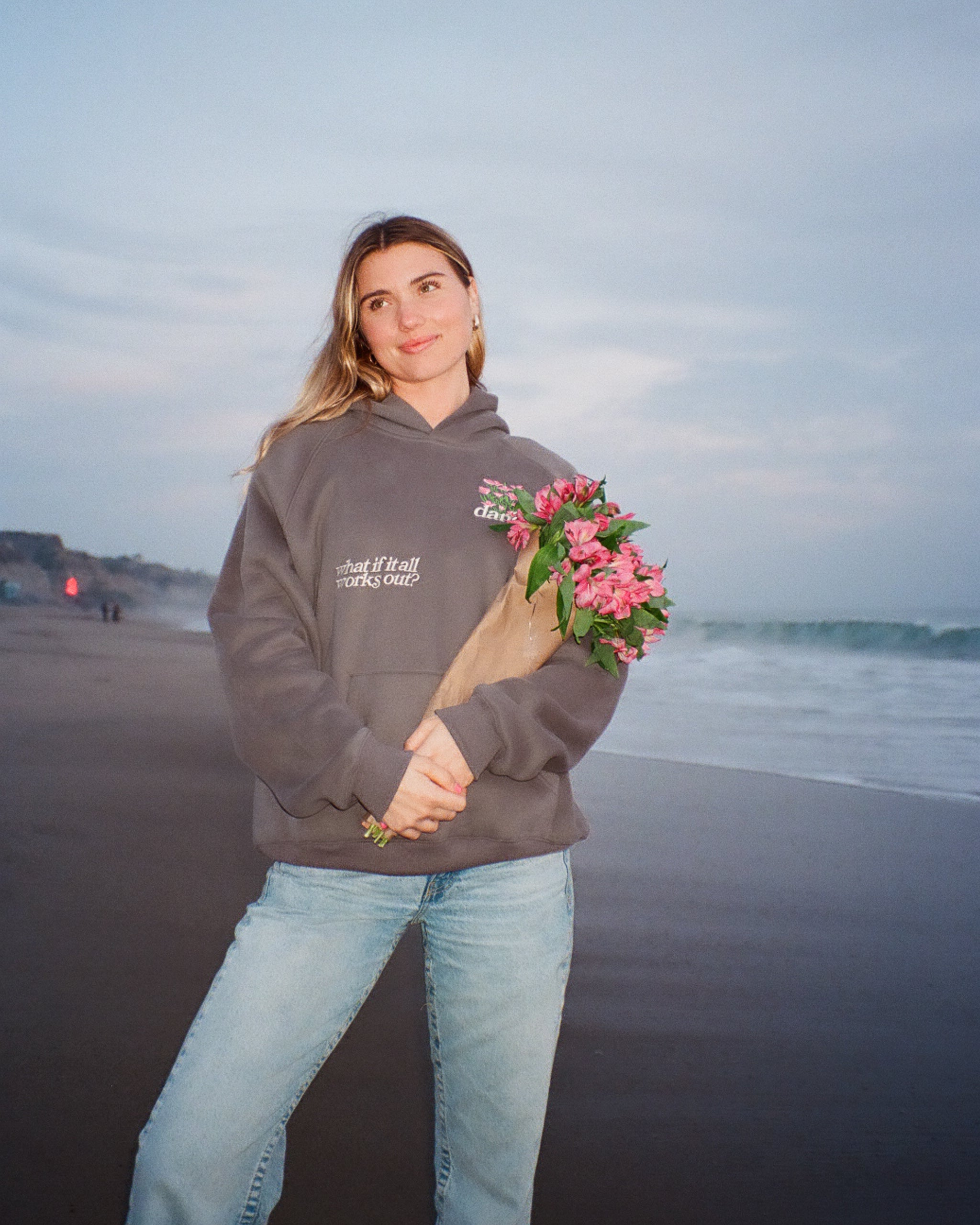 Woman on a beach holding flowers wearing a hoodie with text