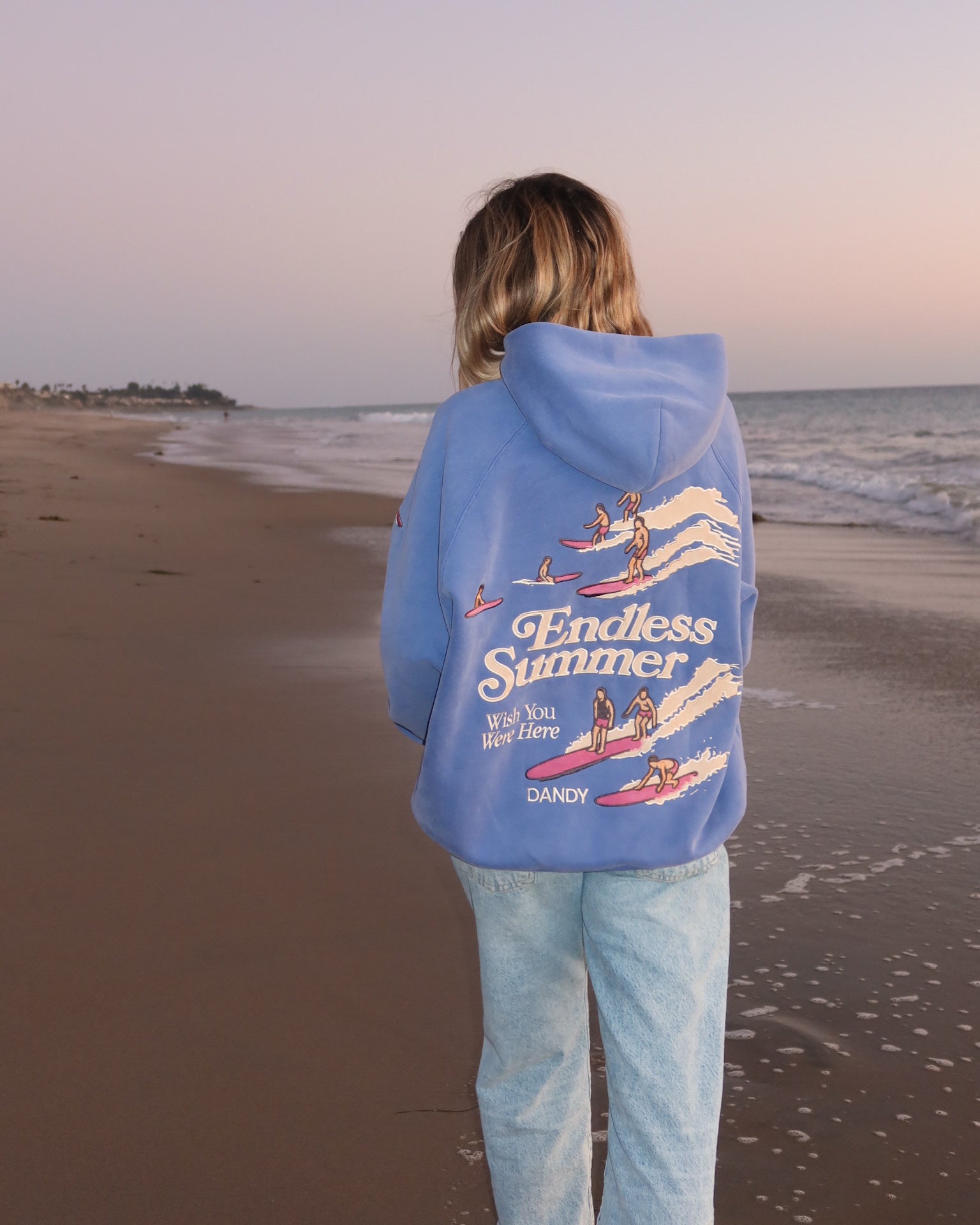 "Endless Summer" Oversized Lux Hoodie in Vintage Washed Blue standing on the beach at sunset