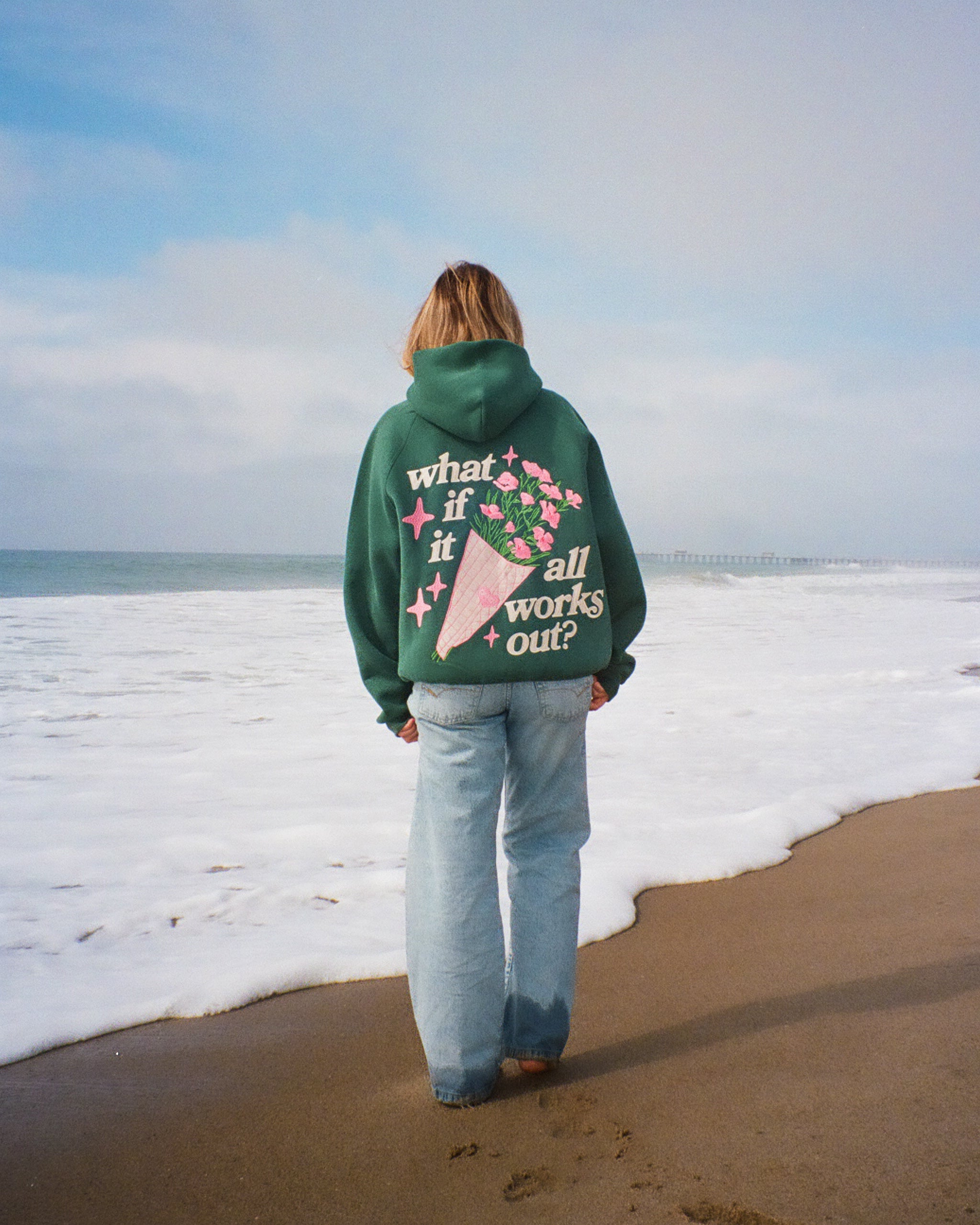 Person wearing a green hoodie with text and graphics on the beach