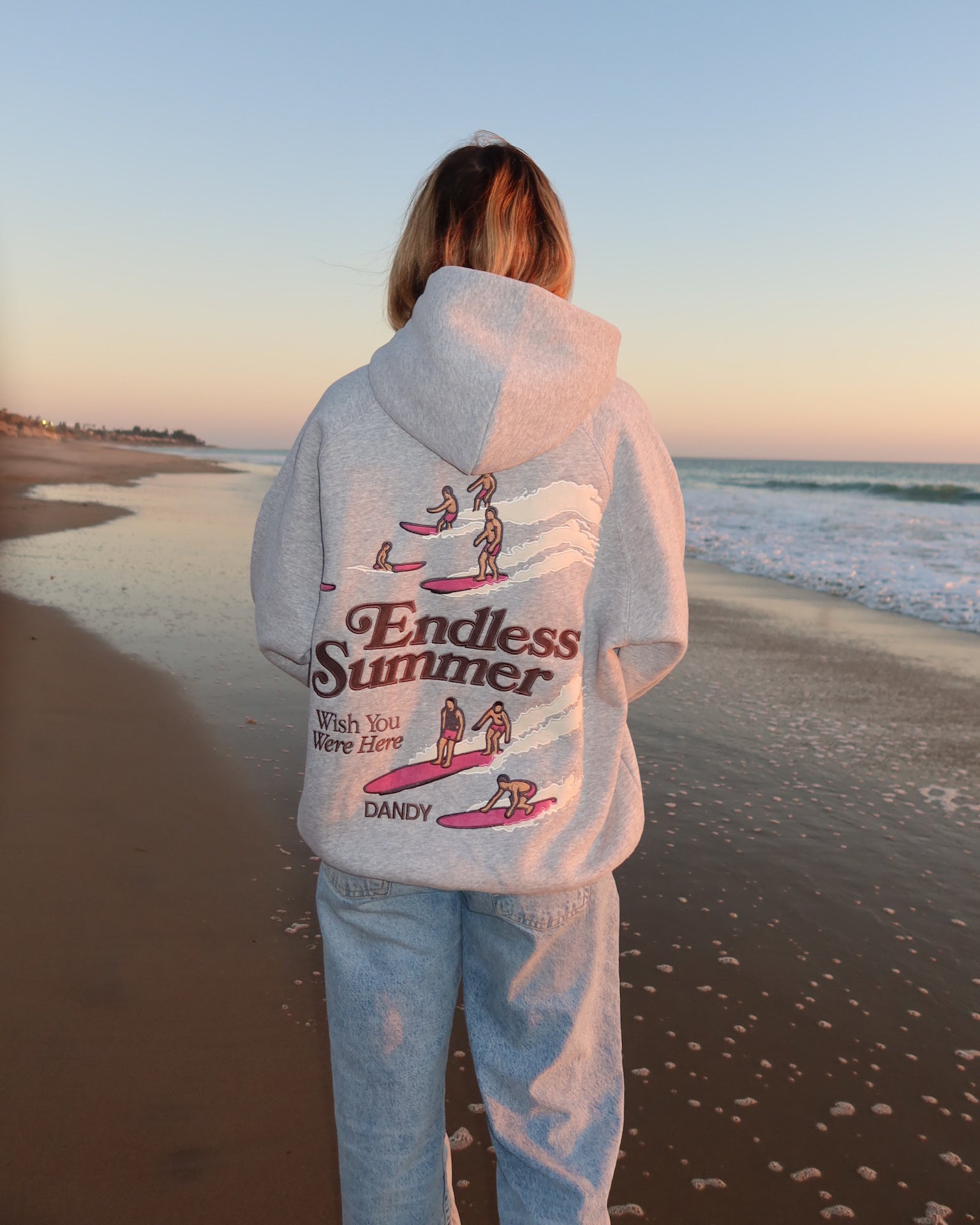 "Endless Summer" Oversized Lux Hoodie in Dark Heather standing on the beach at sunset