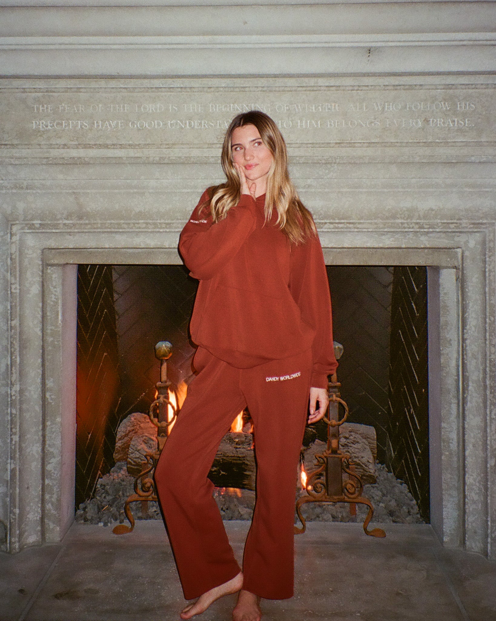 Person wearing a red outfit standing in front of a fireplace with marble surround.