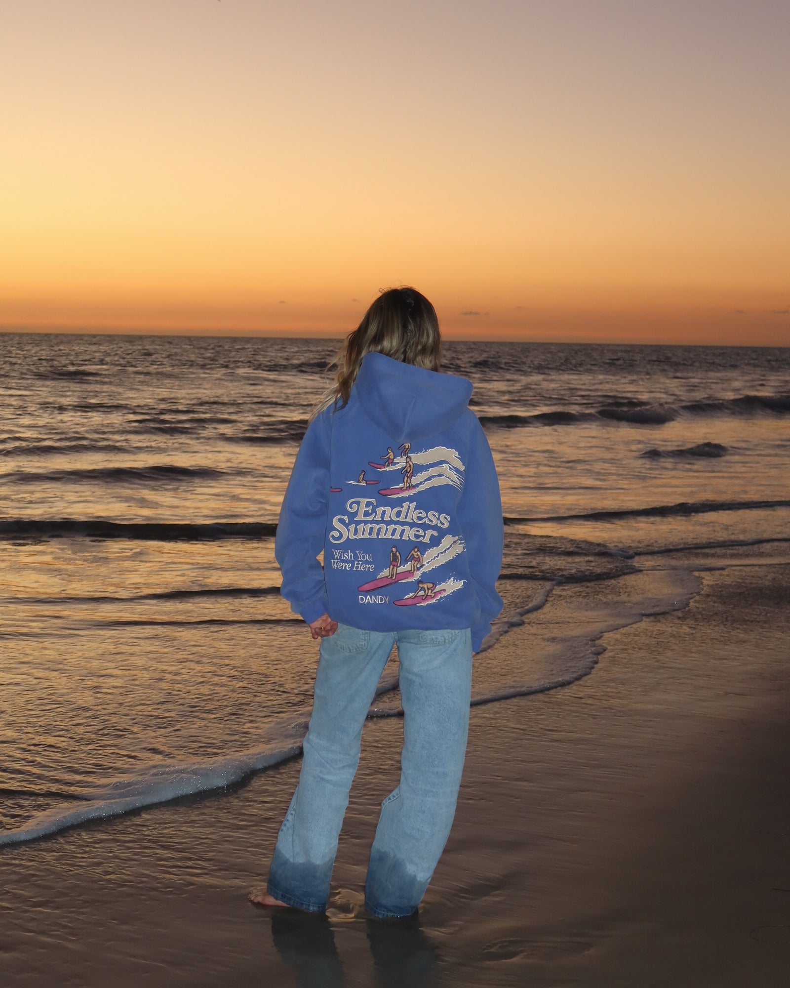 "Endless Summer" Oversized Lux Hoodie in Vintage Washed Blue standing on the beach at sunset