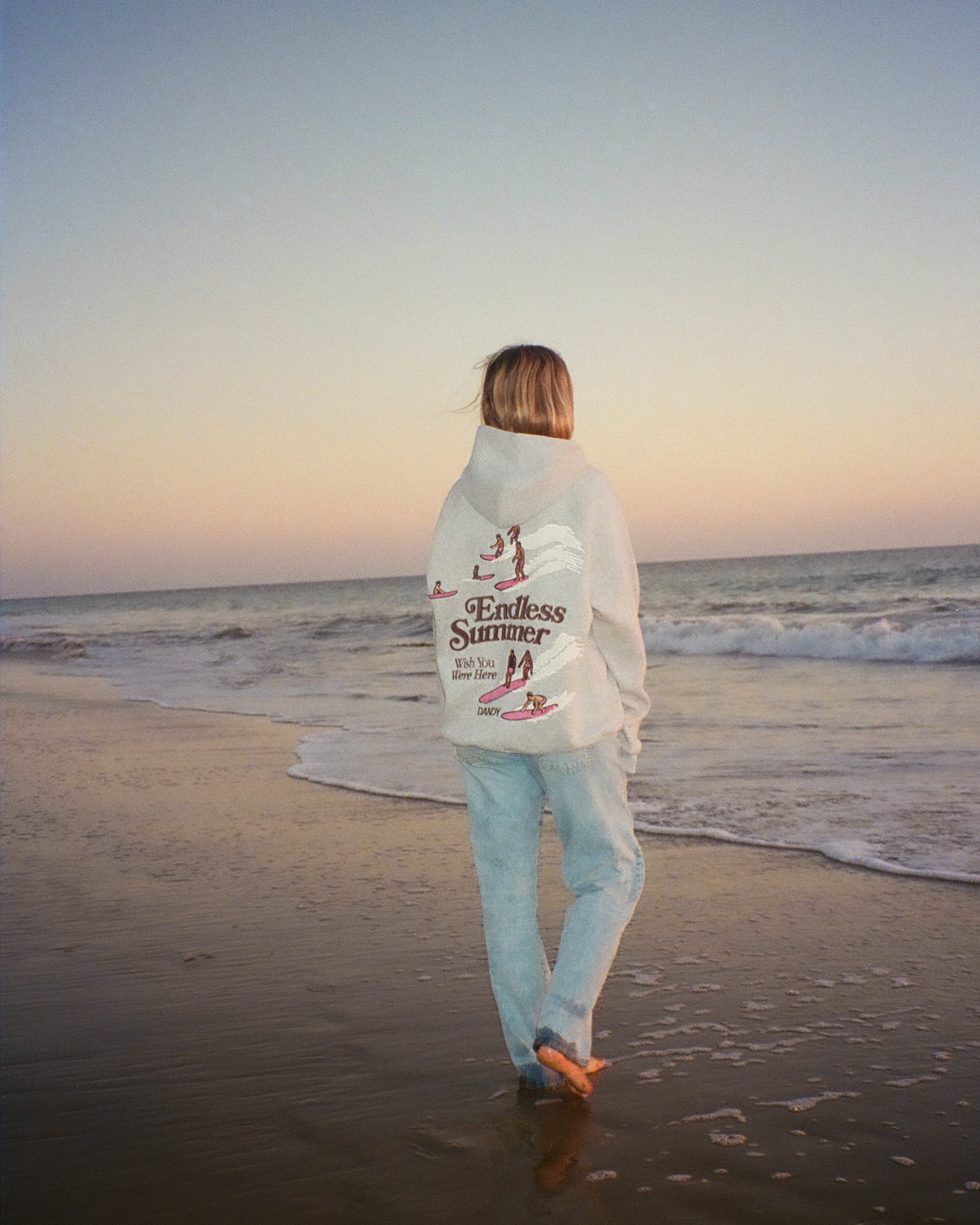"Endless Summer" Oversized Lux Hoodie in Dark Heather walking on the beach at sunset
