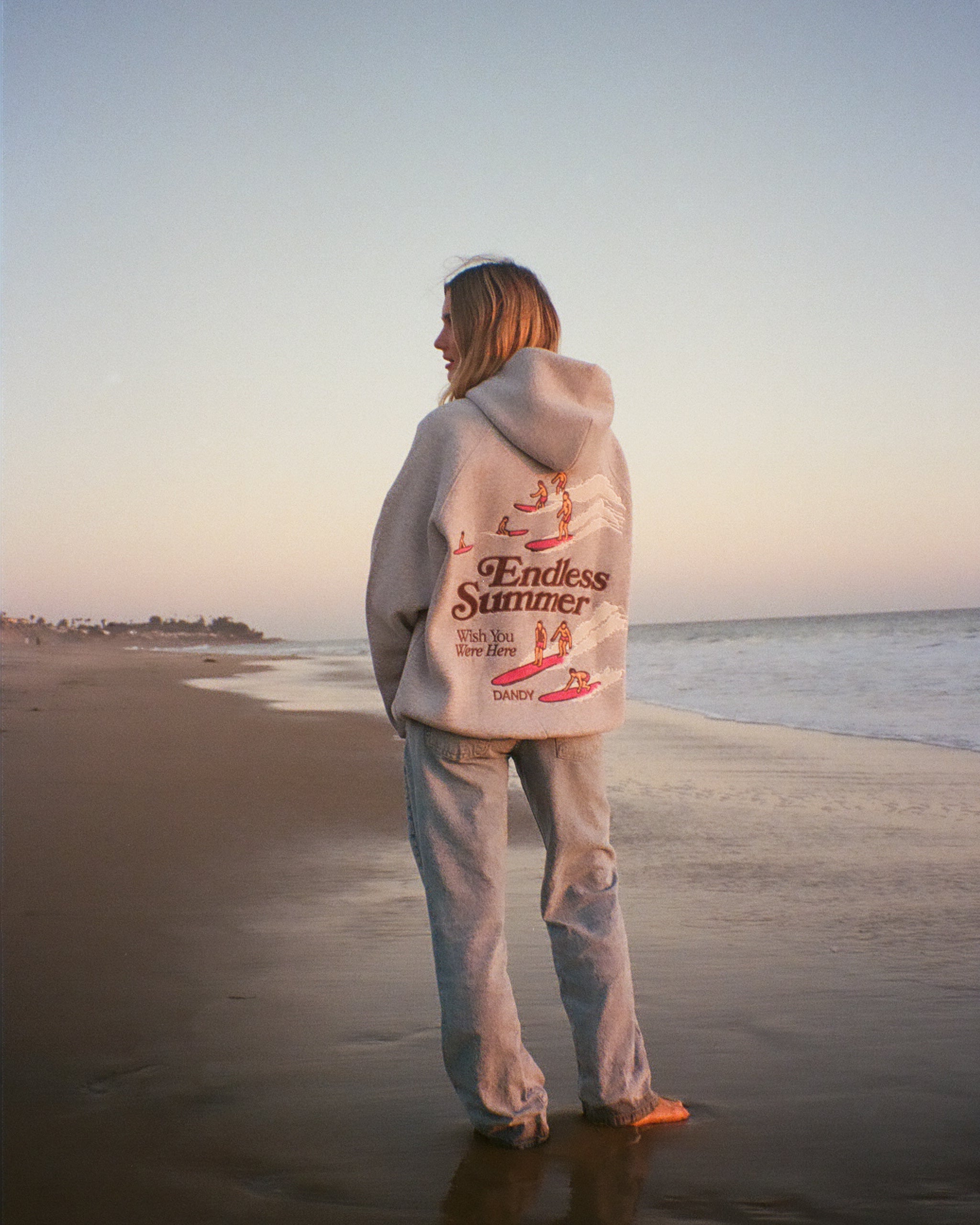 "Endless Summer" Oversized Lux Hoodie in Dark Heather standing on the beach at sunset