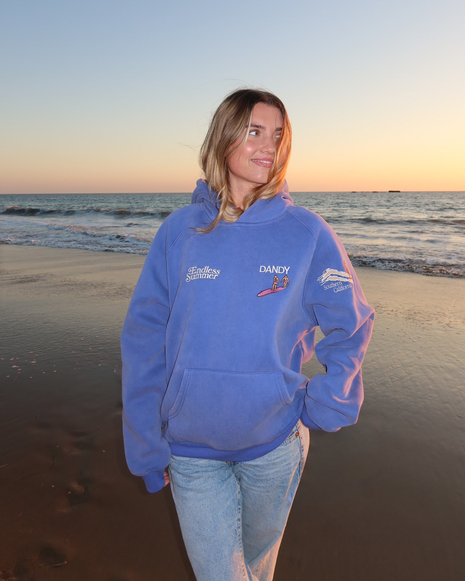 "Endless Summer" Oversized Lux Hoodie in Vintage Washed Blue showing the front of the hoodie on the beach at sunset