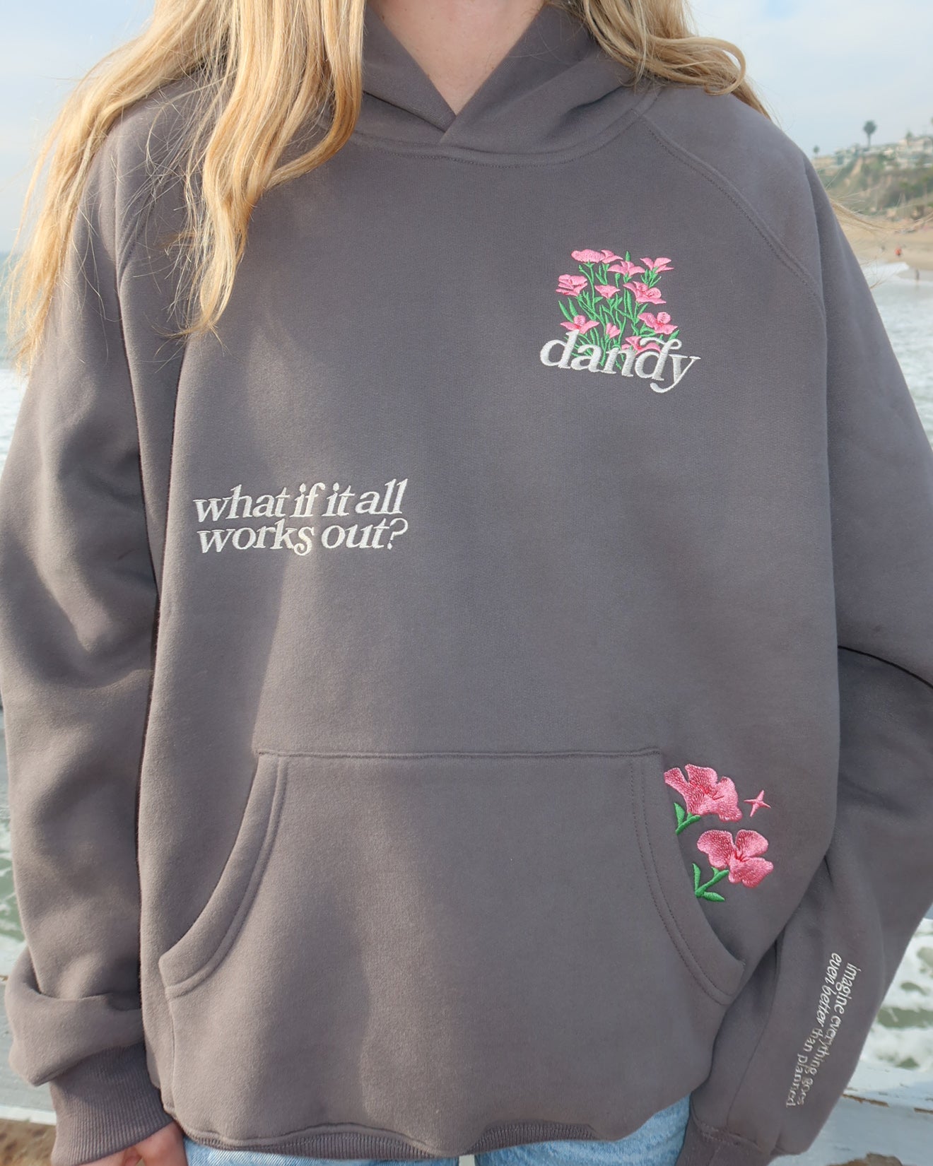 Person wearing a gray hoodie with floral designs and text, standing outdoors.