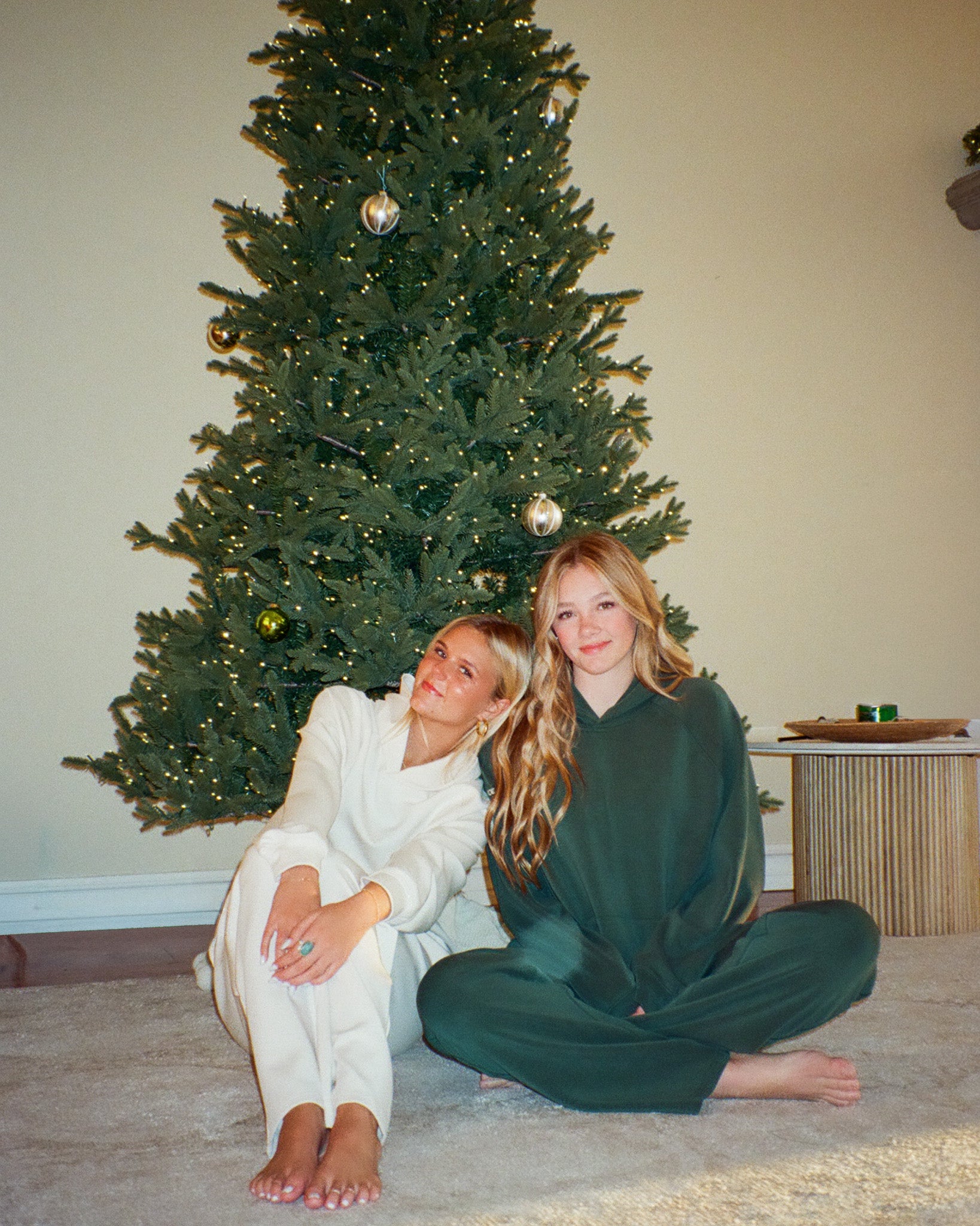 Two women sitting on the floor in front of a decorated Christmas tree.