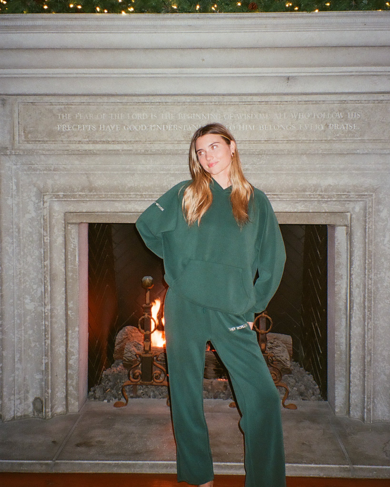 Person wearing a green tracksuit standing in front of a fireplace.