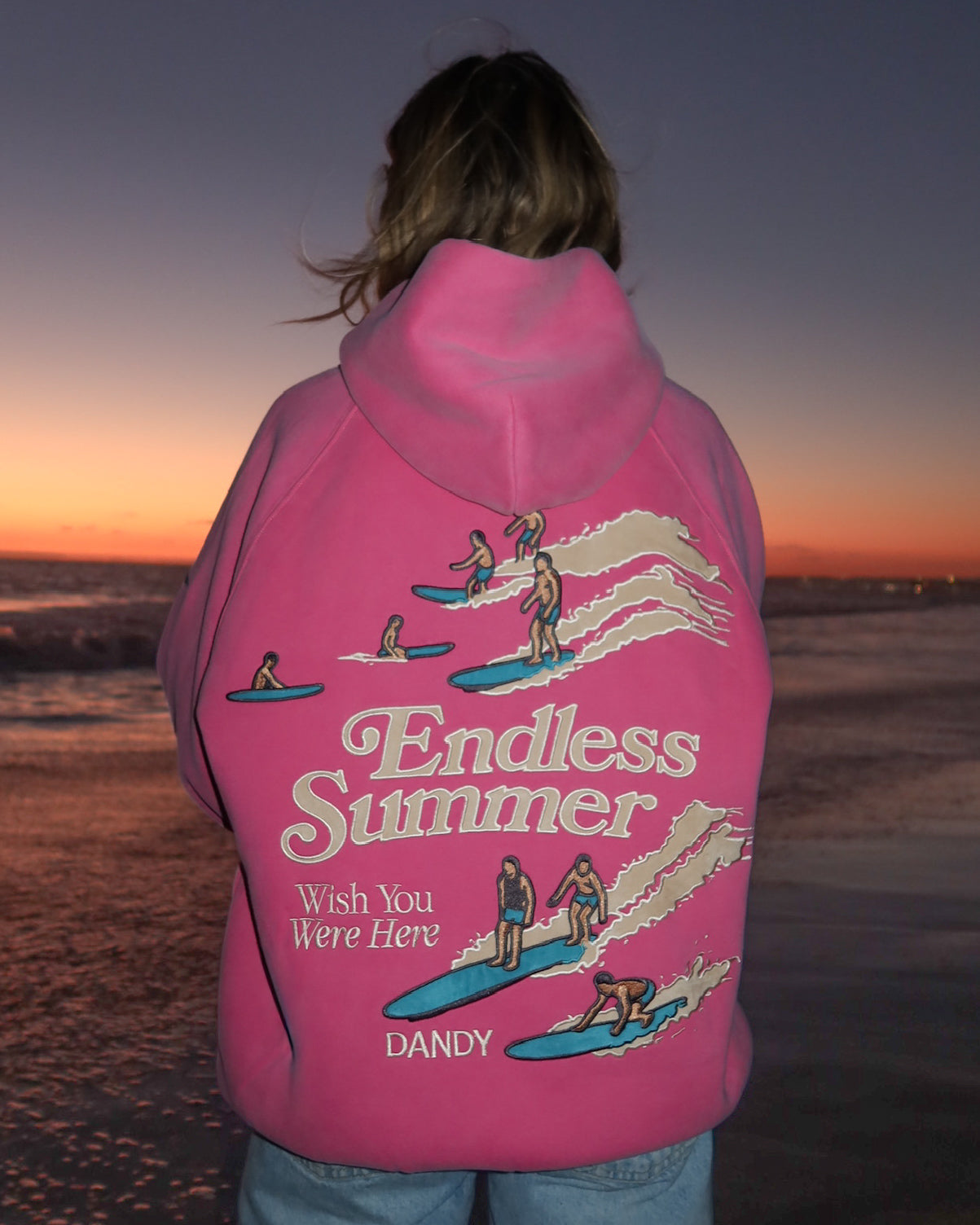"Endless Summer" Oversized Lux Hoodie in Vintage Washed Pink standing on a sandy beach at sunset