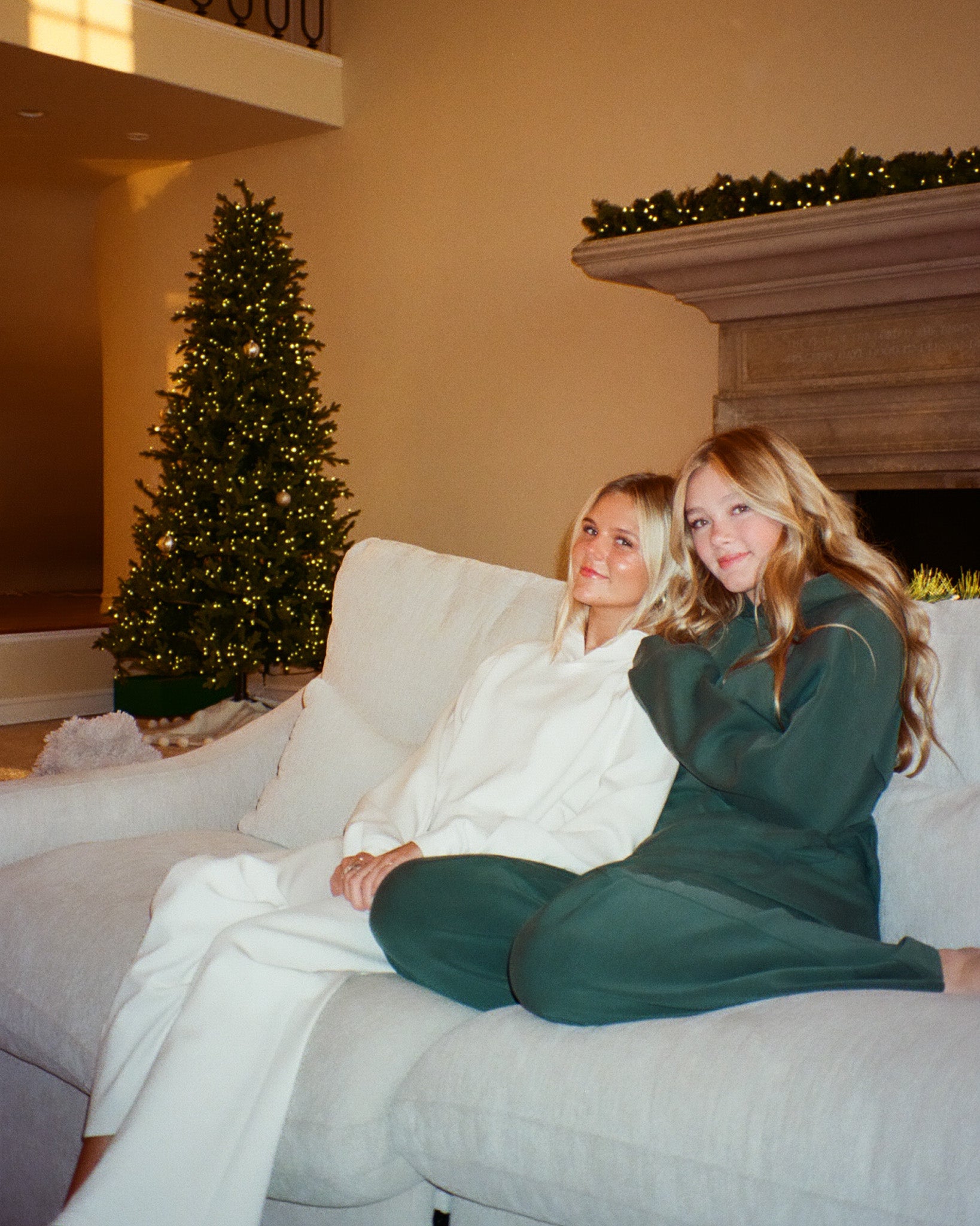 Two women sitting on a couch in a living room with Christmas decorations.