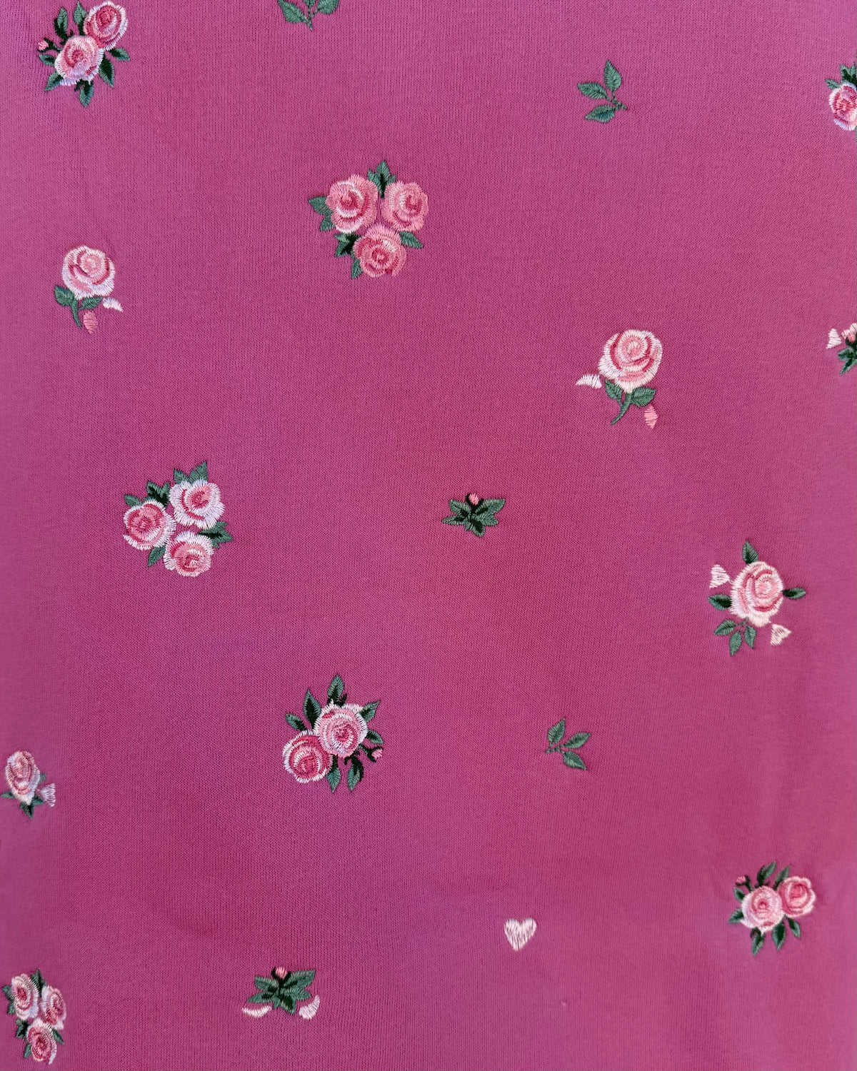 A close-up of a pink fabric with a repeating pattern of small pink roses and green leaves.