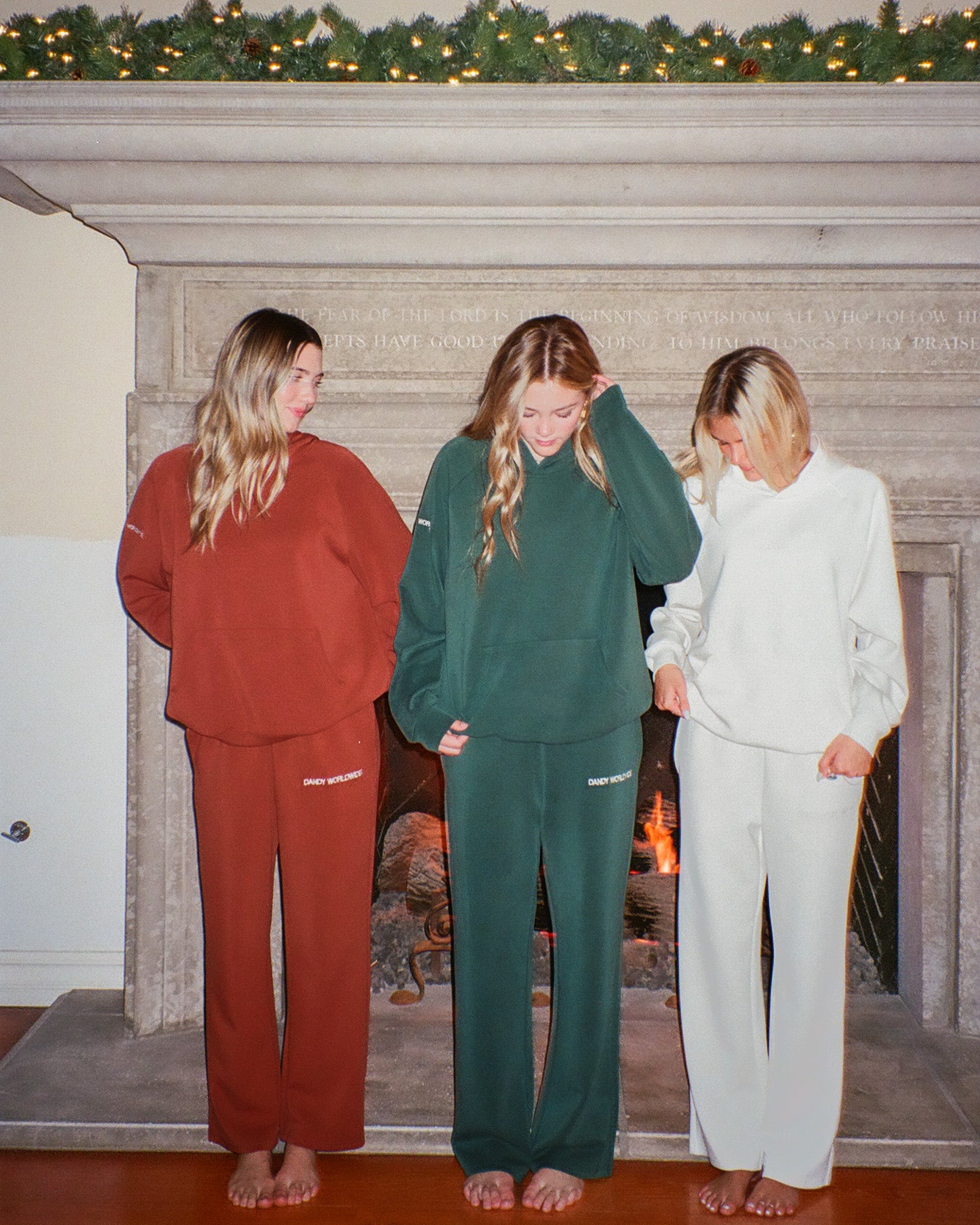Three people wearing matching tracksuits in front of a fireplace.