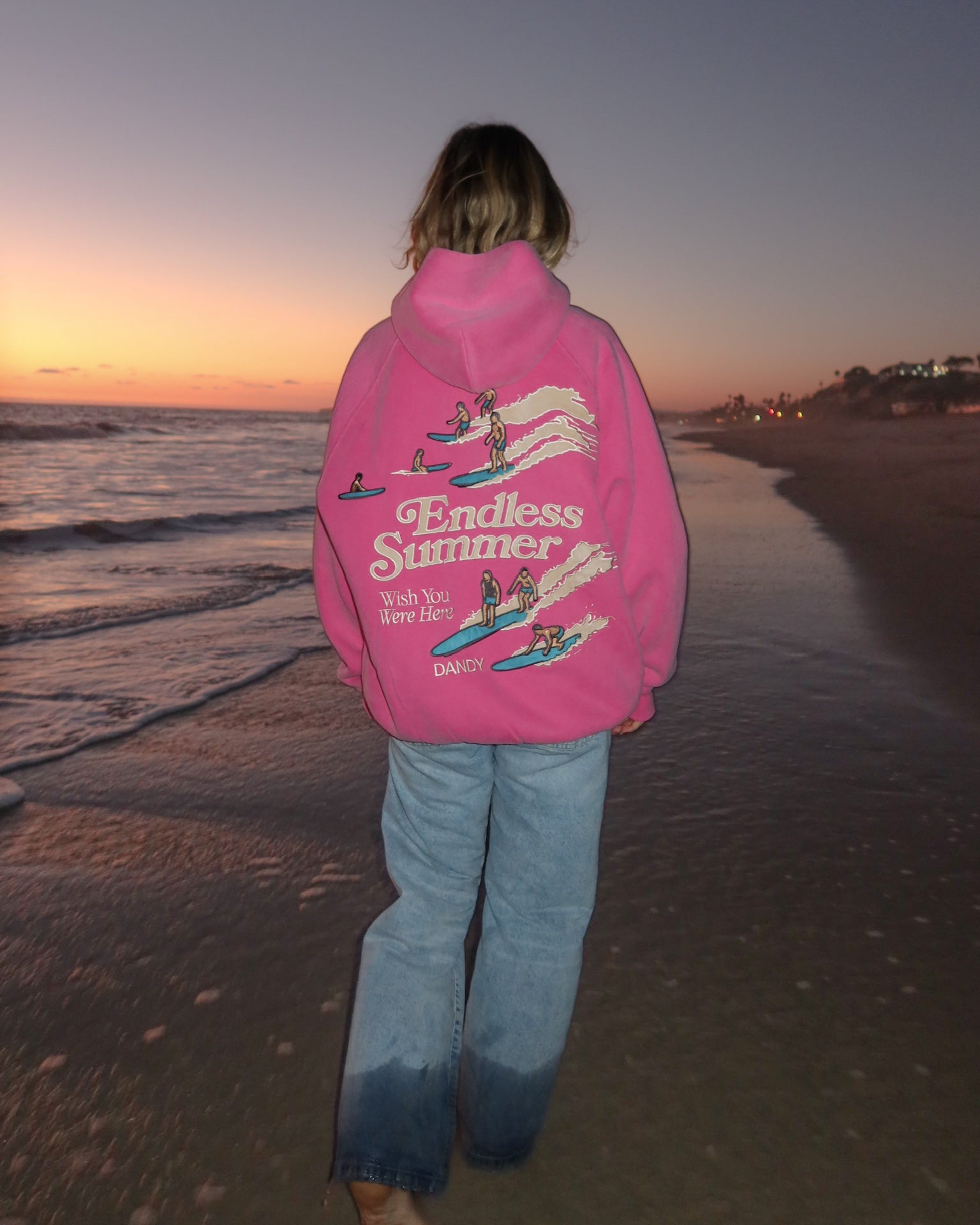 "Endless Summer" Oversized Lux Hoodie in Vintage Washed Pink walking away while on the beach at sunset