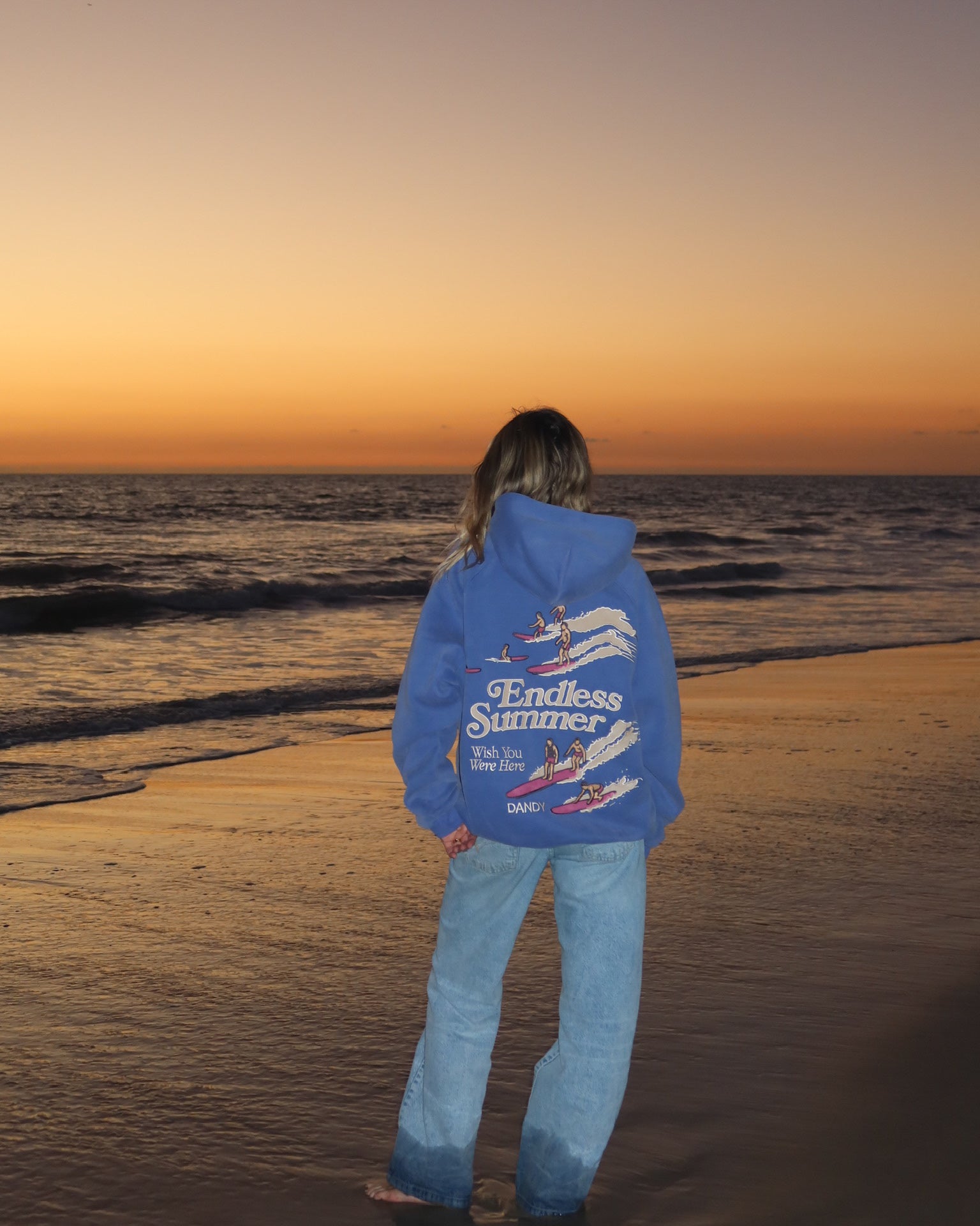 "Endless Summer" Oversized Lux Hoodie in Vintage Washed Blue standing on the beach at sunset
