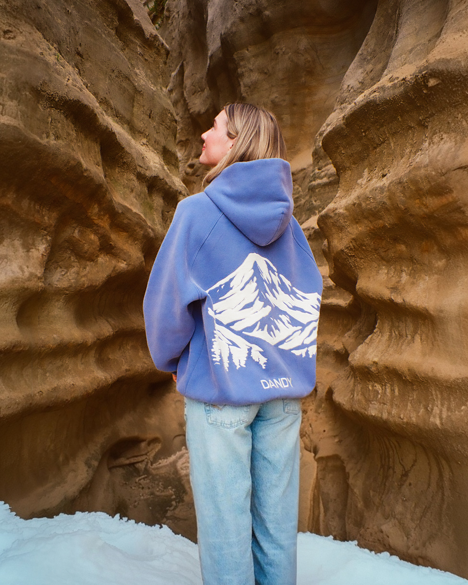 Person wearing a blue hoodie with a mountain design in a rocky canyon.