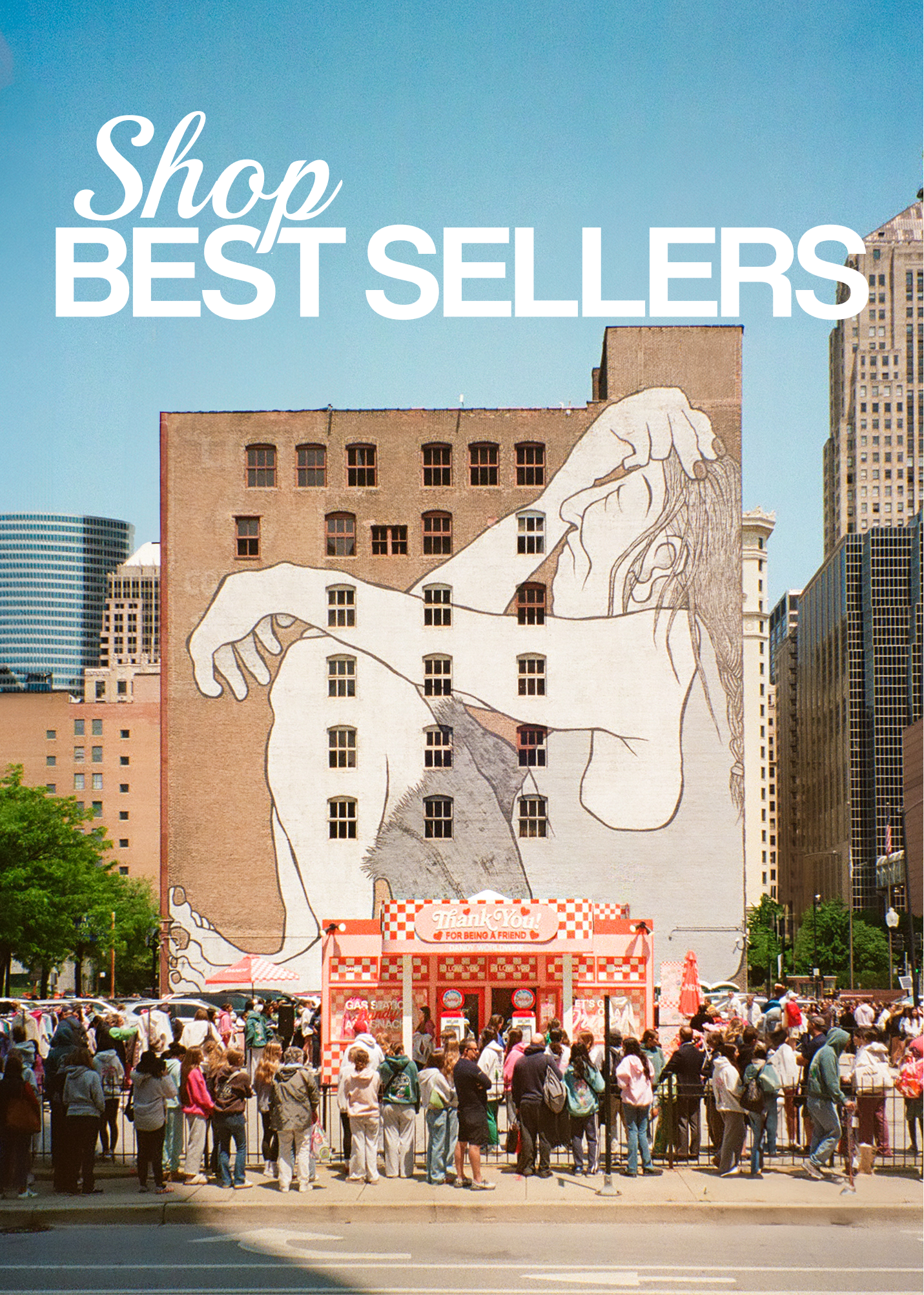 CLICKABLE IMAGE THAT READS: SHOP BEST SELLERS.
An image from Dandy's Chicago Popup. Behind is Mural on a building with people gathered below in an urban setting