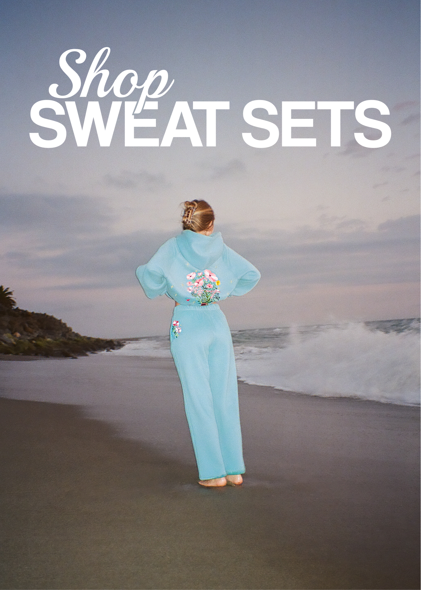 Clickable image with text overlay that reads  'Shop Sweat Sets'. Person in a light blue sweat set standing on a beach.