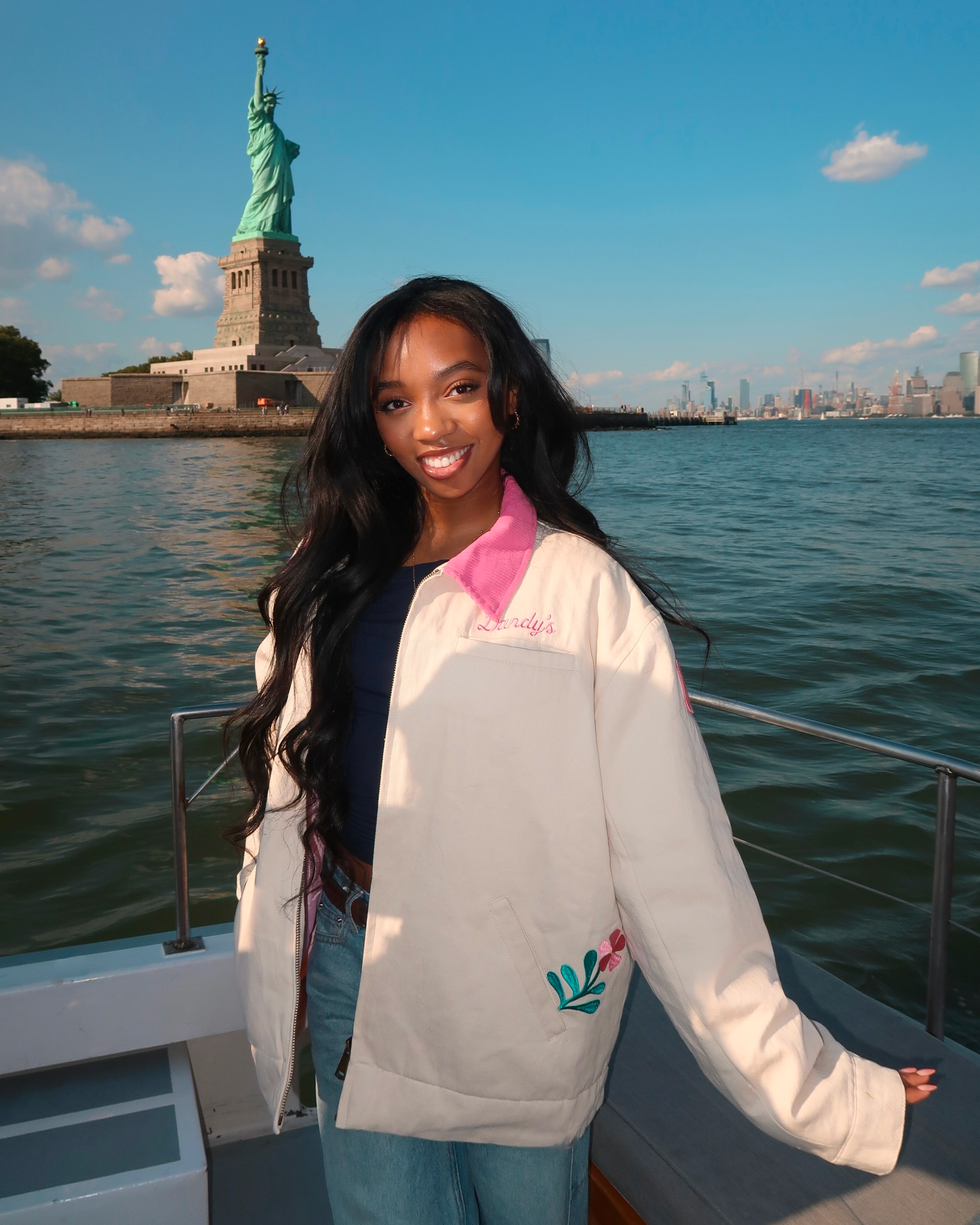 Woman posing in front of the Statue of Liberty on a boat wearing a cream jacket.