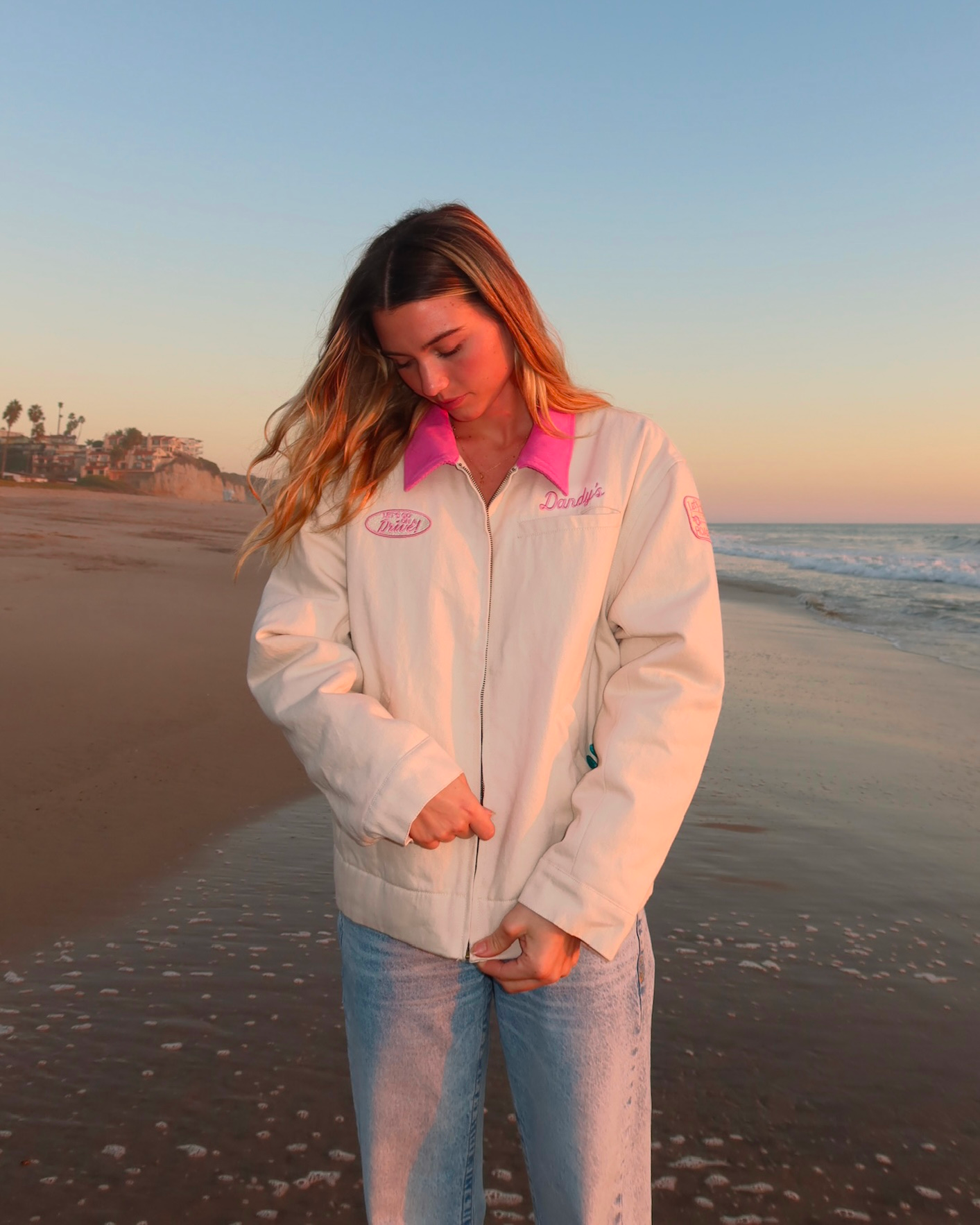 Person wearing a white jacket with a logo on a beach at sunset