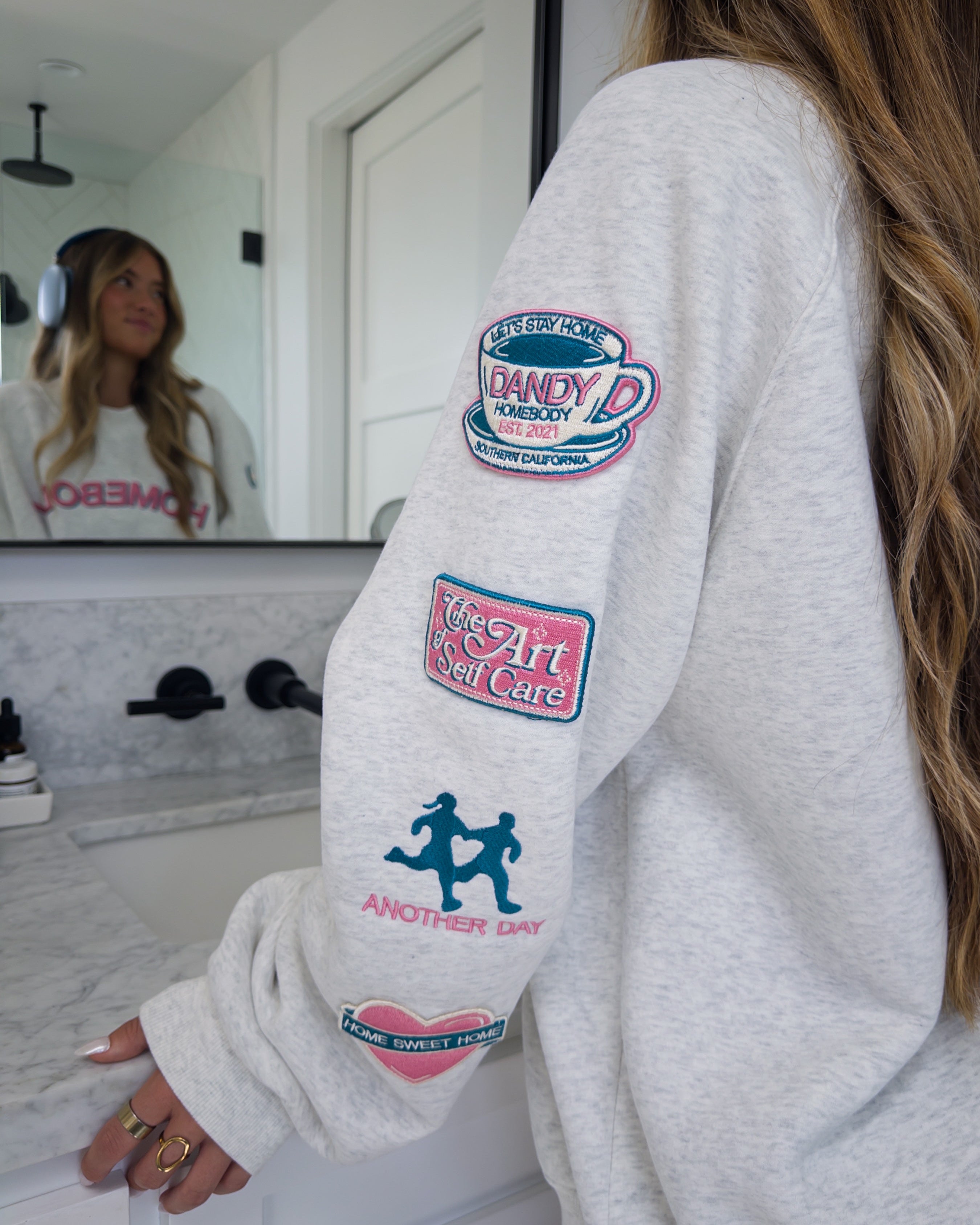 Person wearing a white sweatshirt with colorful patches in a bathroom.