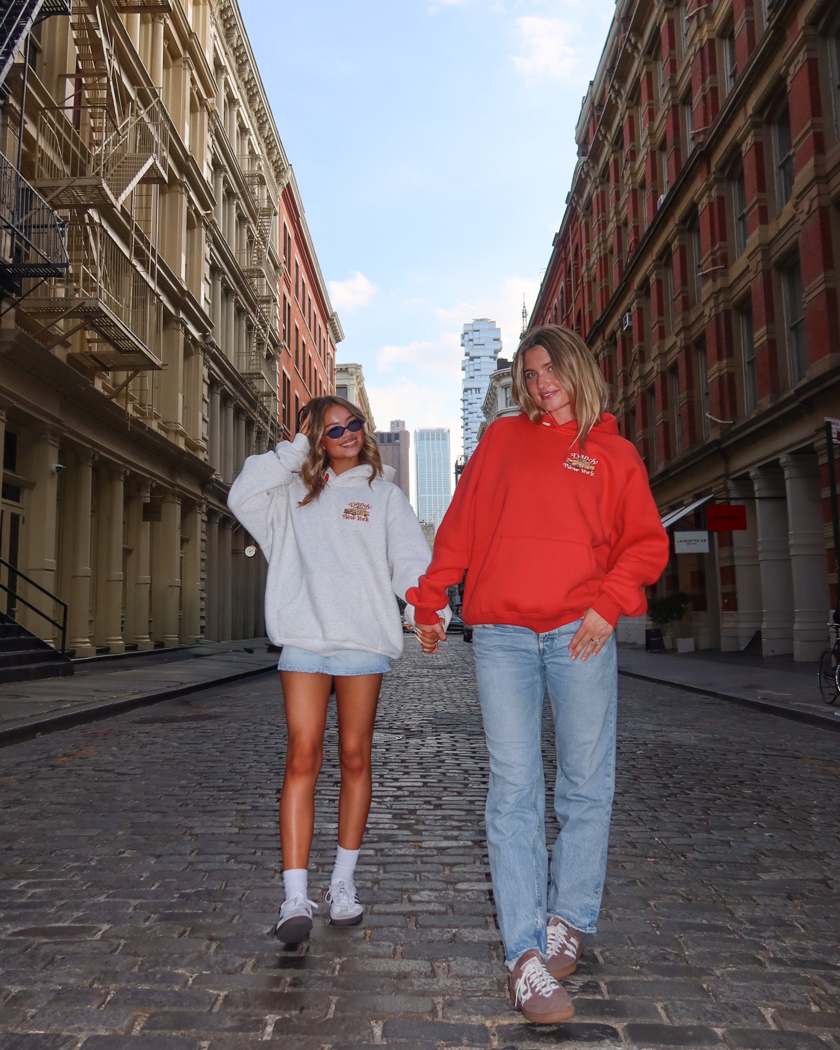 Two people walking down a street in an urban setting, wearing matching hoodies.