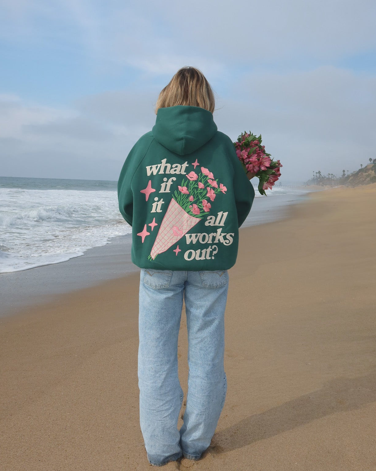 Person wearing a green hoodie with text and graphics on a beach