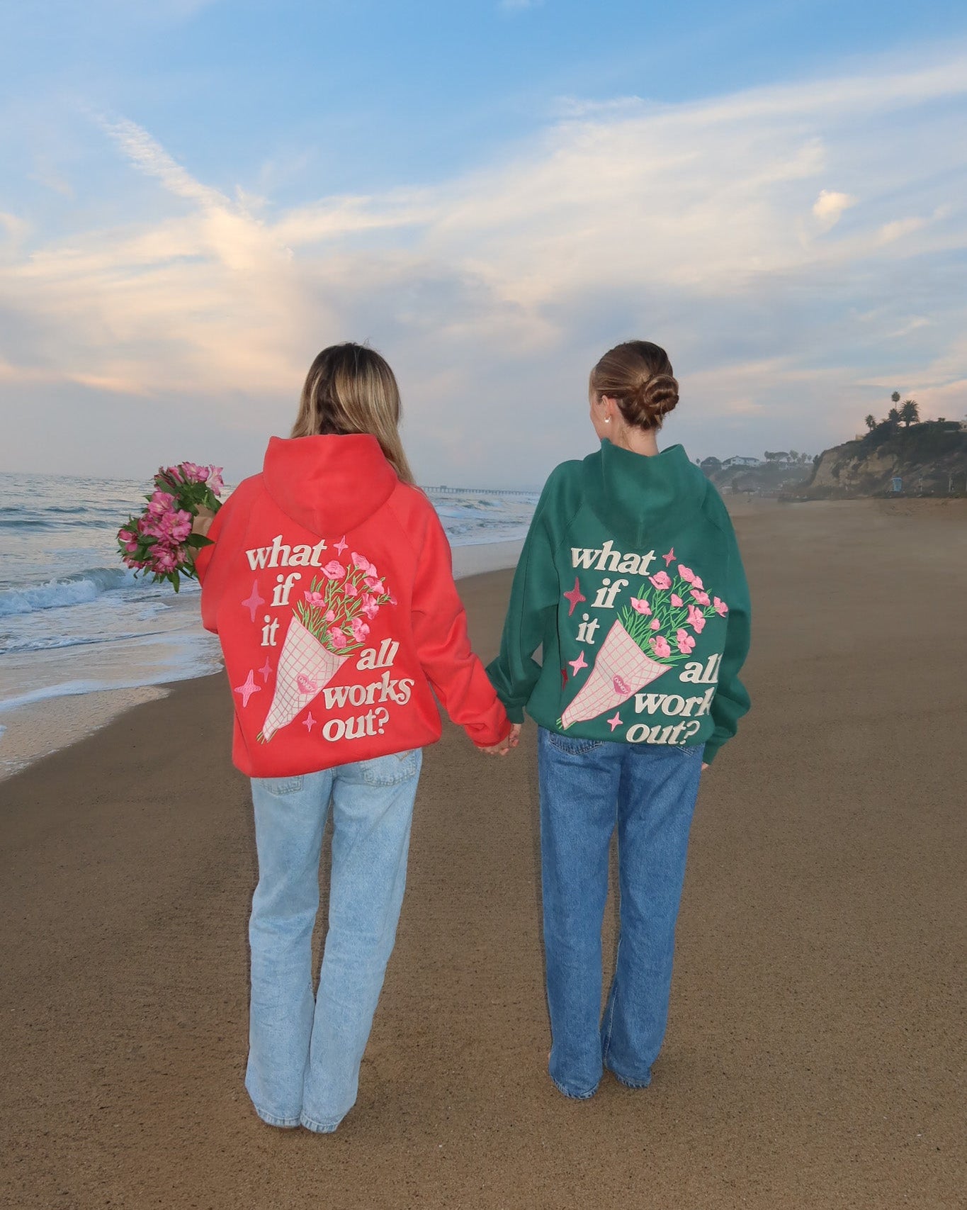 Two people standing on a beach wearing red and green hoodies with text and graphics.
