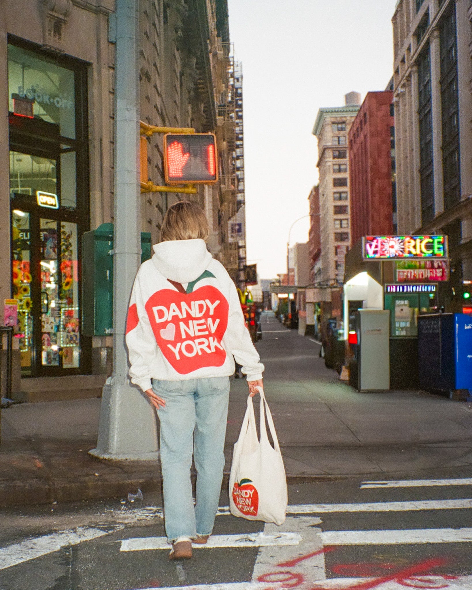 Person wearing a white hoodie with a red heart design walking on a city street.