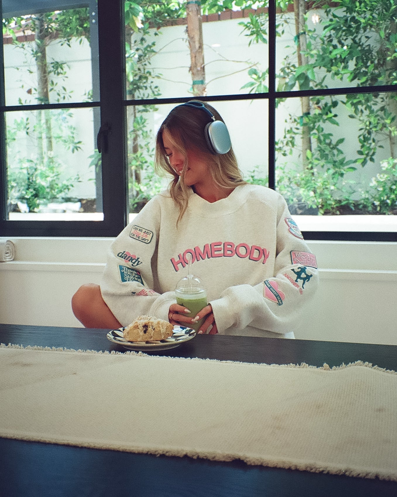 Girl wearing a 'Homebody' sweatshirt at a kitchen table with a drink and dessert.