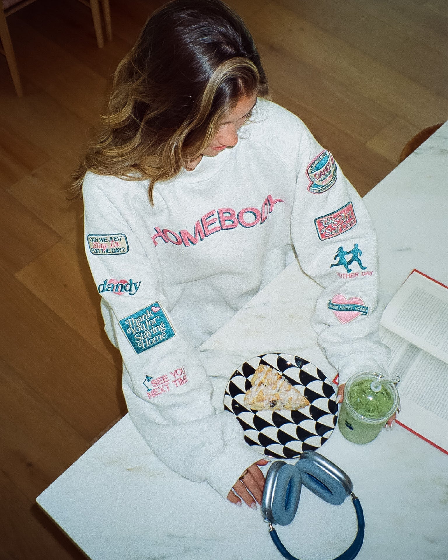 Person wearing a white sweatshirt with various patches sitting at a table with a plate of food and a drink.