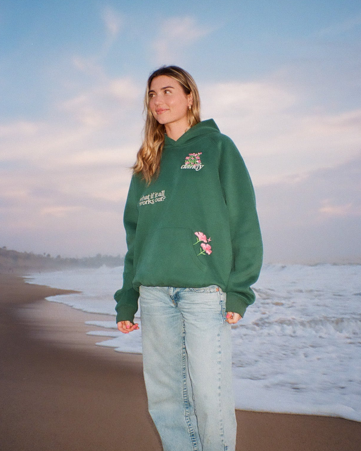 Person wearing a green hoodie with floral designs on a beach