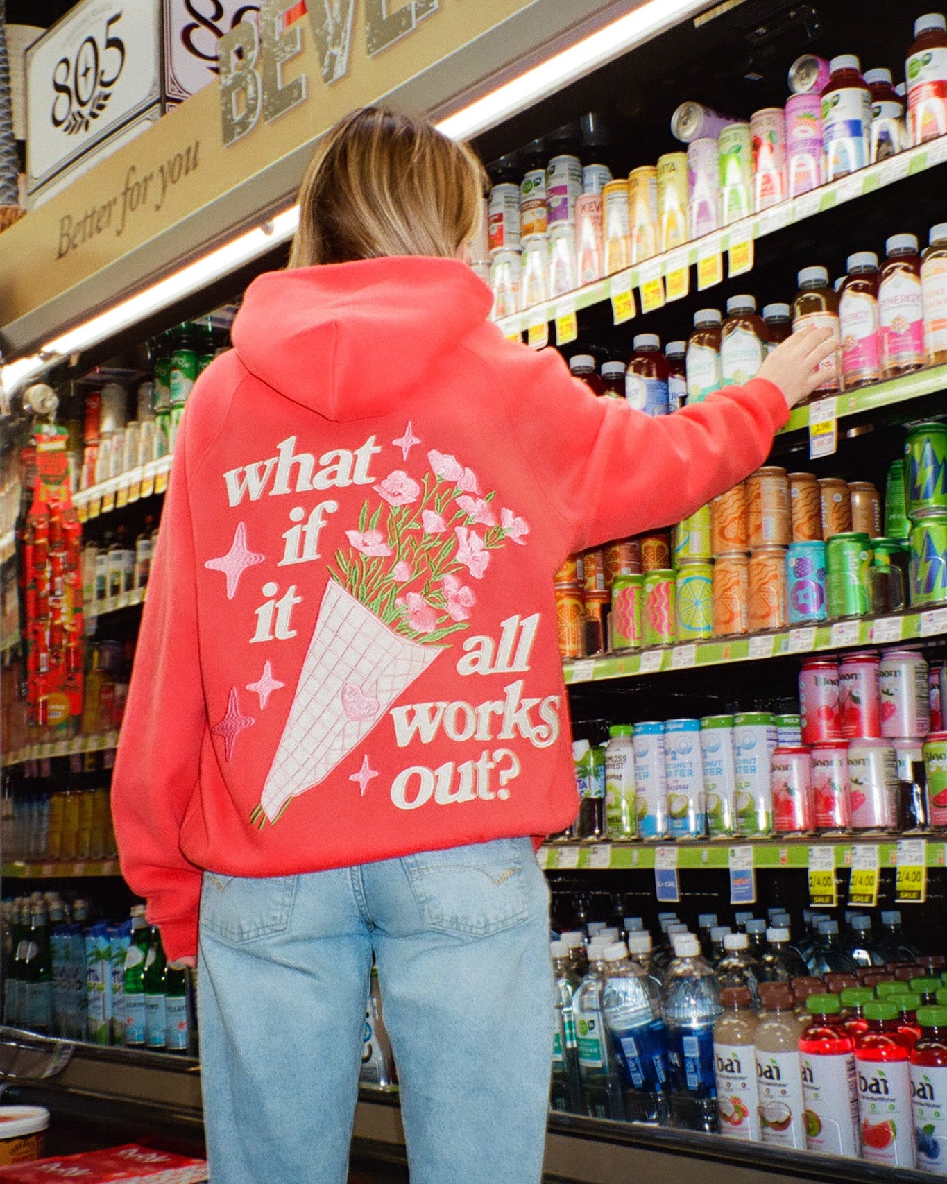 Person wearing a red hoodie with a floral design and text in a grocery store.