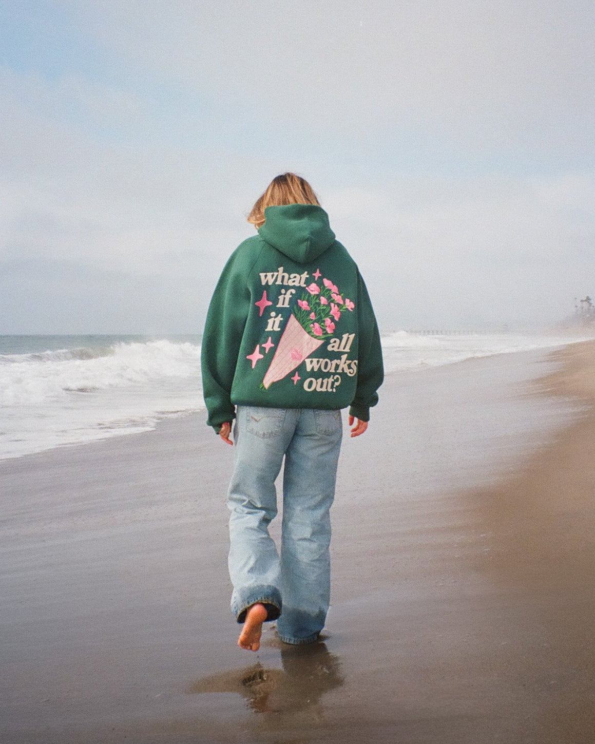 Person wearing a green hoodie with text walking on a beach