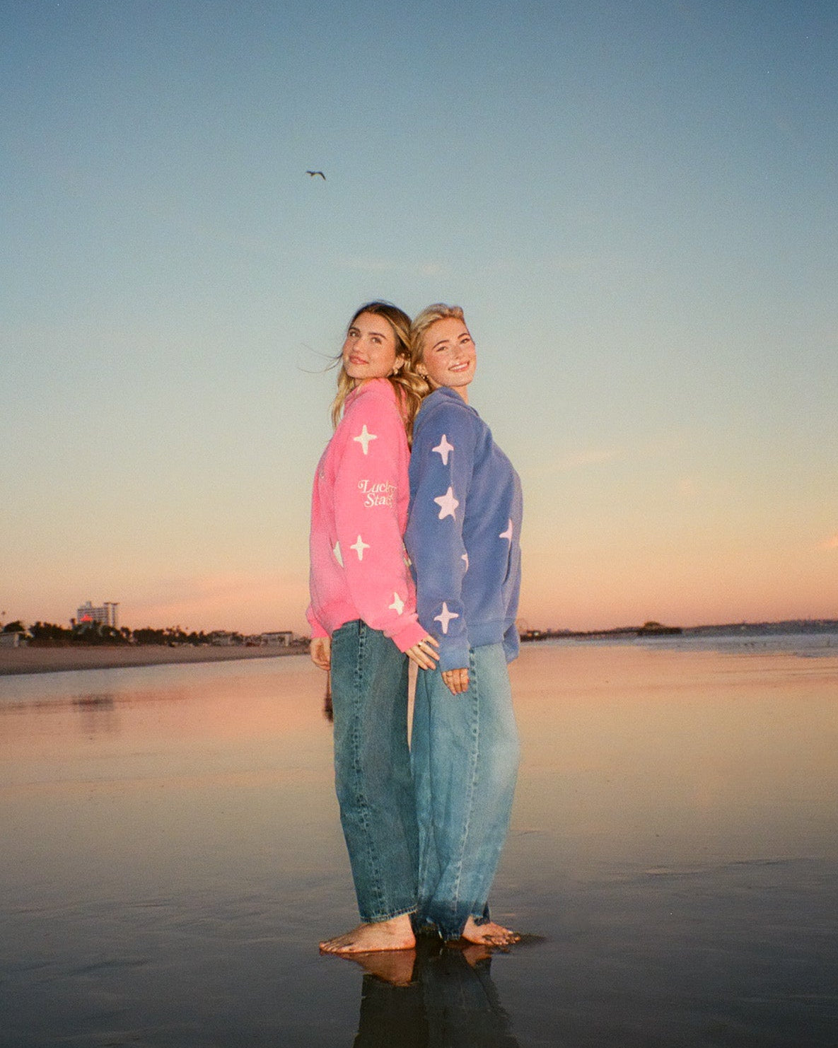 Two people standing on a beach at sunset, wearing colorful shirts with star patterns.