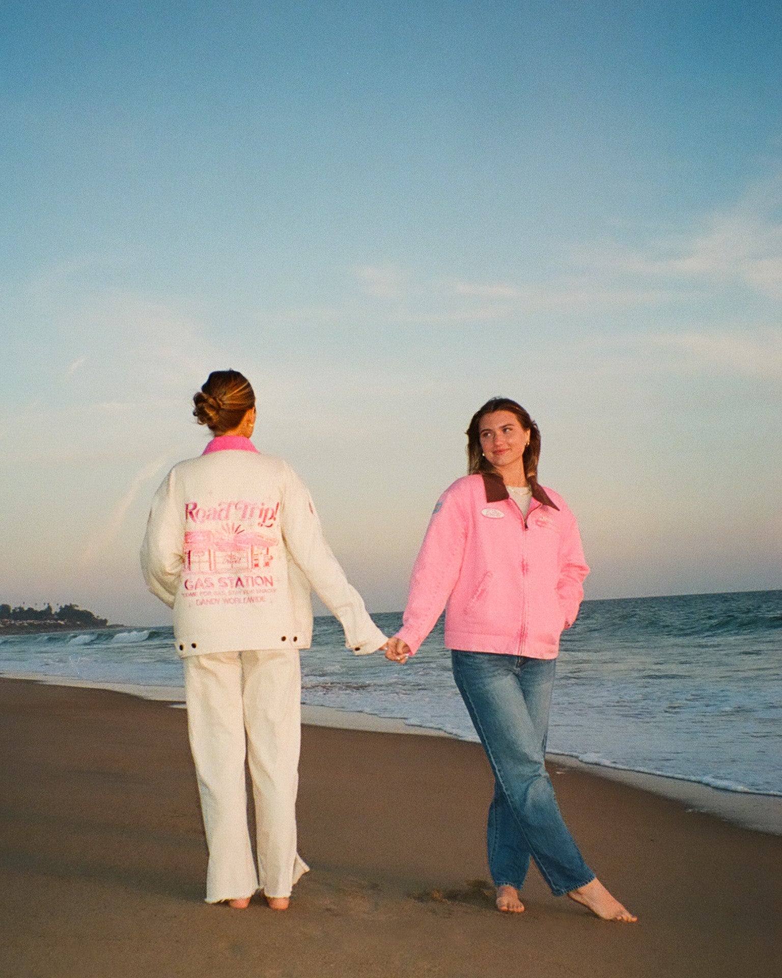 Two people holding hands on a beach at sunset.