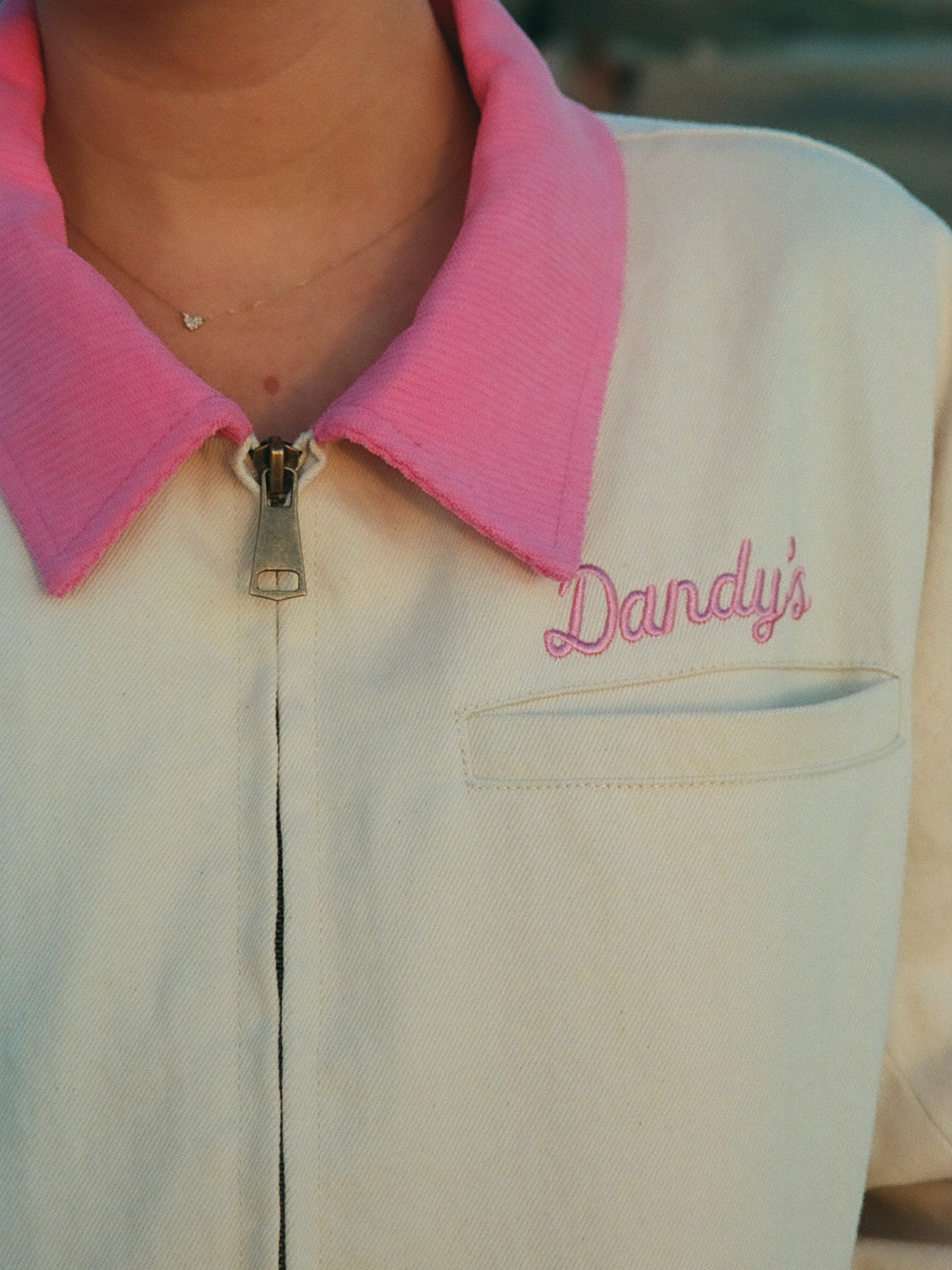Close-up of a beige jacket with pink collar and 'Dandy's' embroidery.