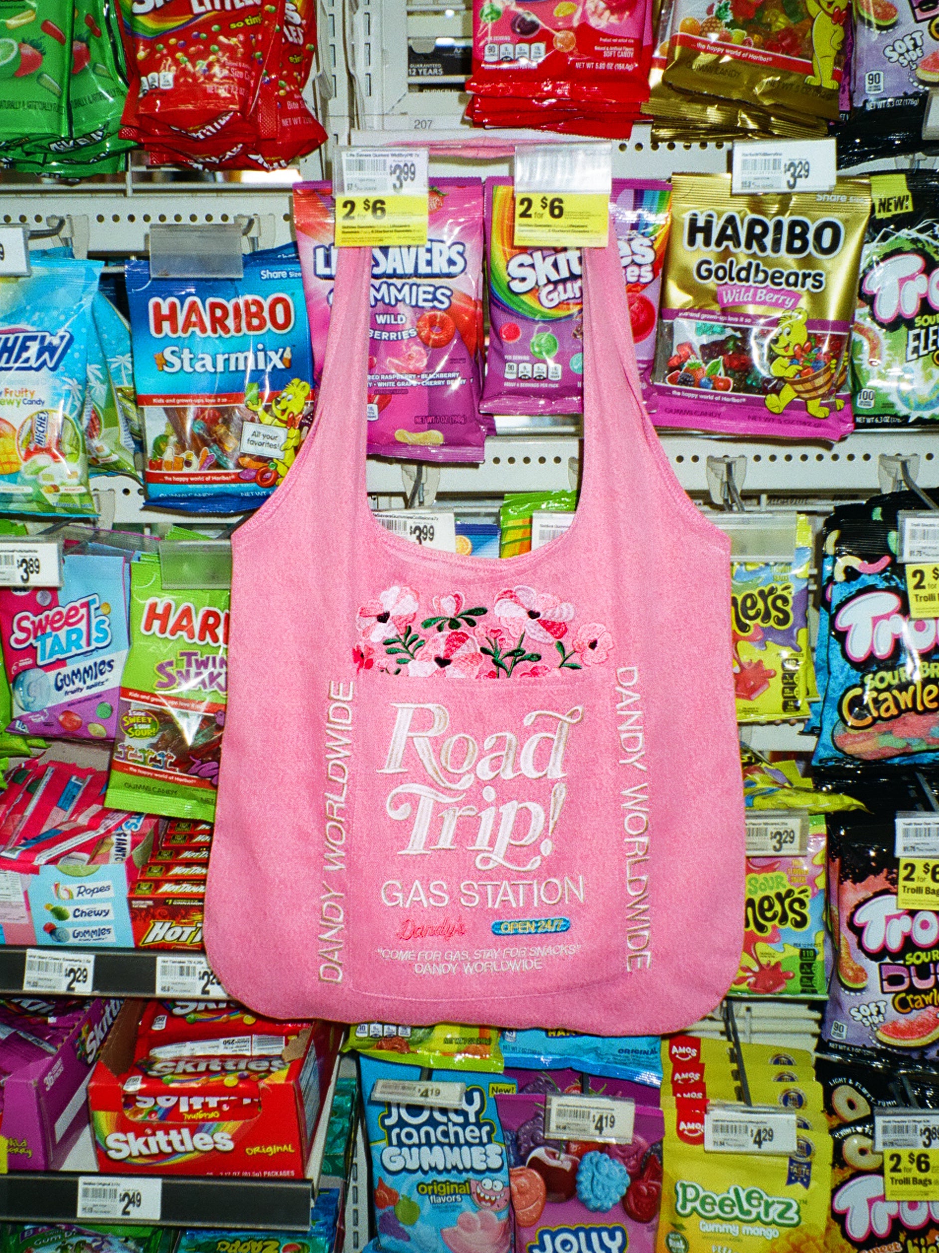 Pink reusable denim tote bag with 'Road Trip' text in a candy store setting