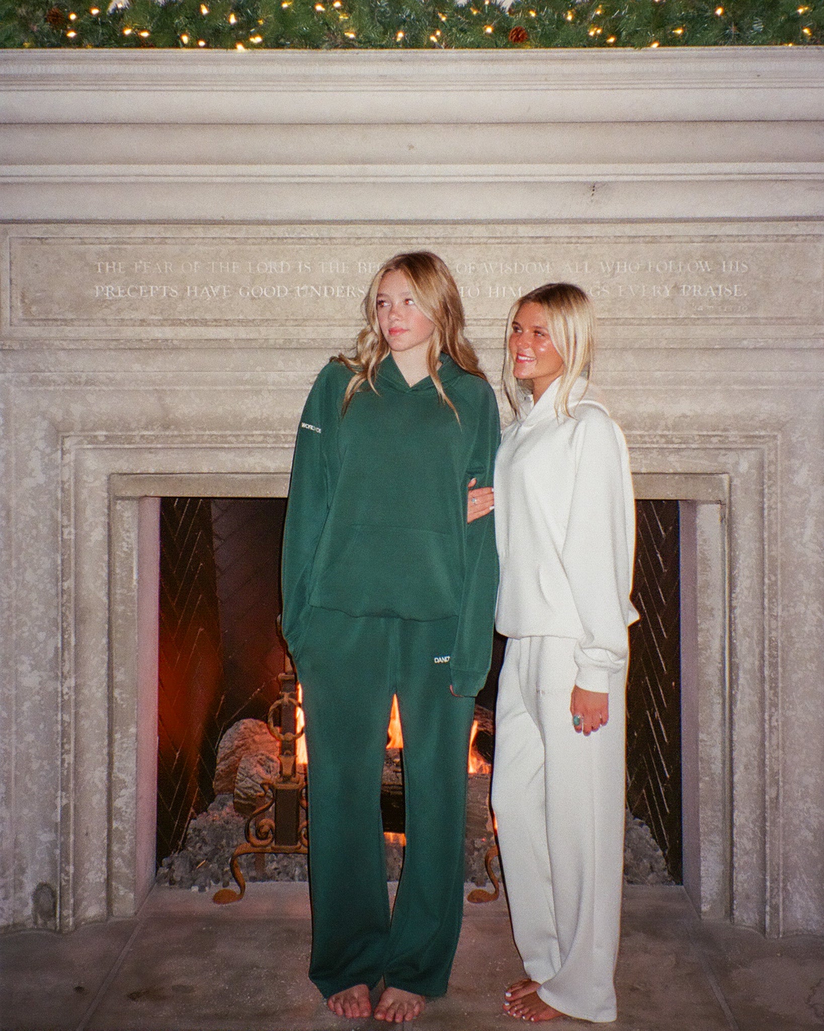 Two women in matching green and white outfits standing in front of a stone fireplace.