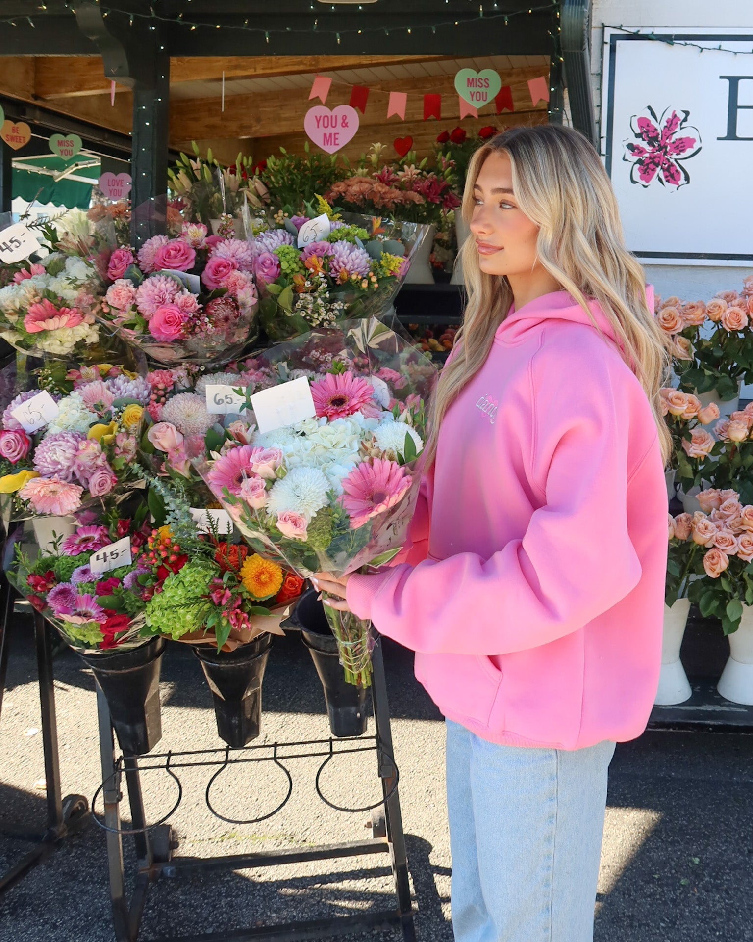 Woman in a pink hoodie holding flowers at a flower market