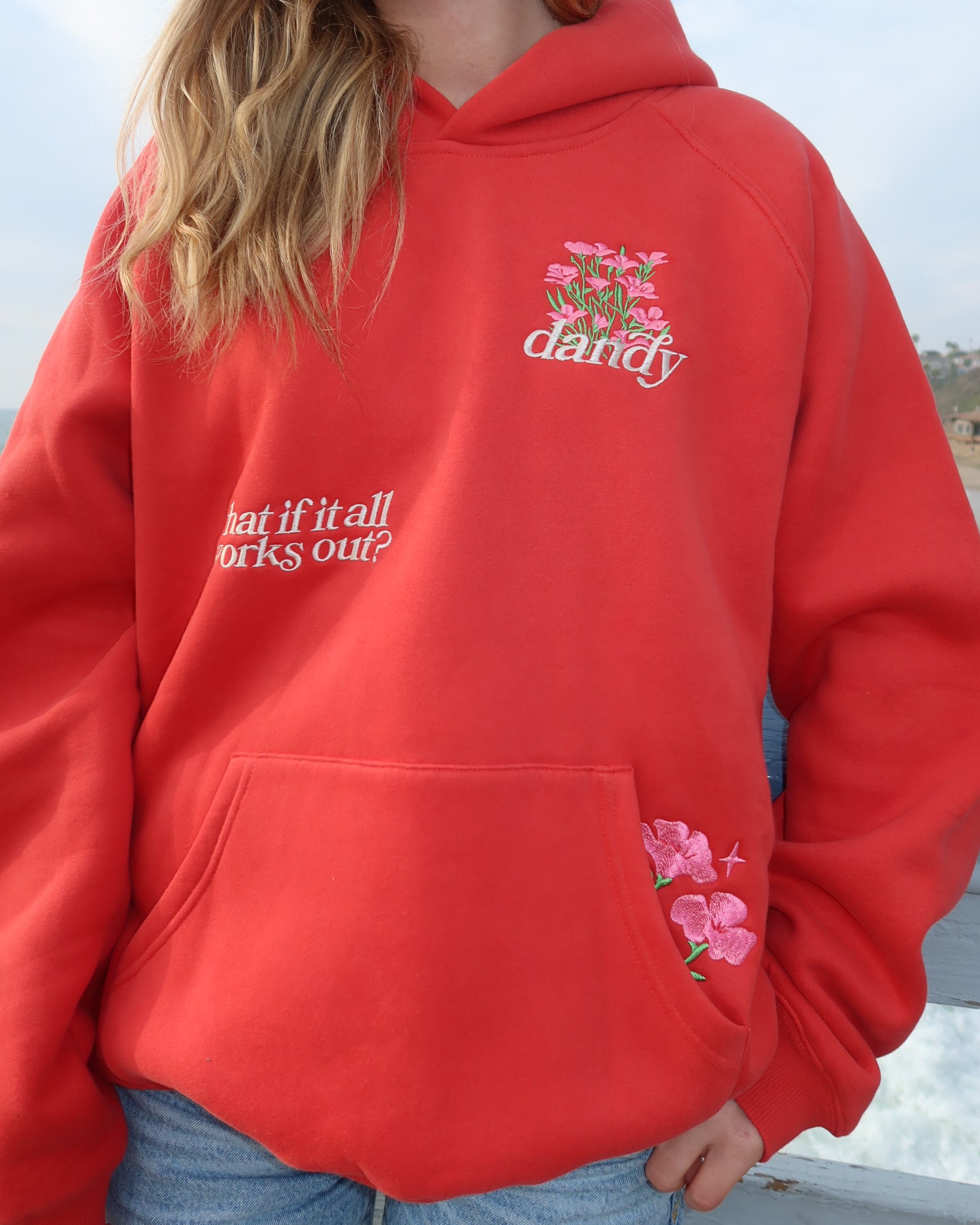 Red hoodie with floral design and text worn by a person outdoors