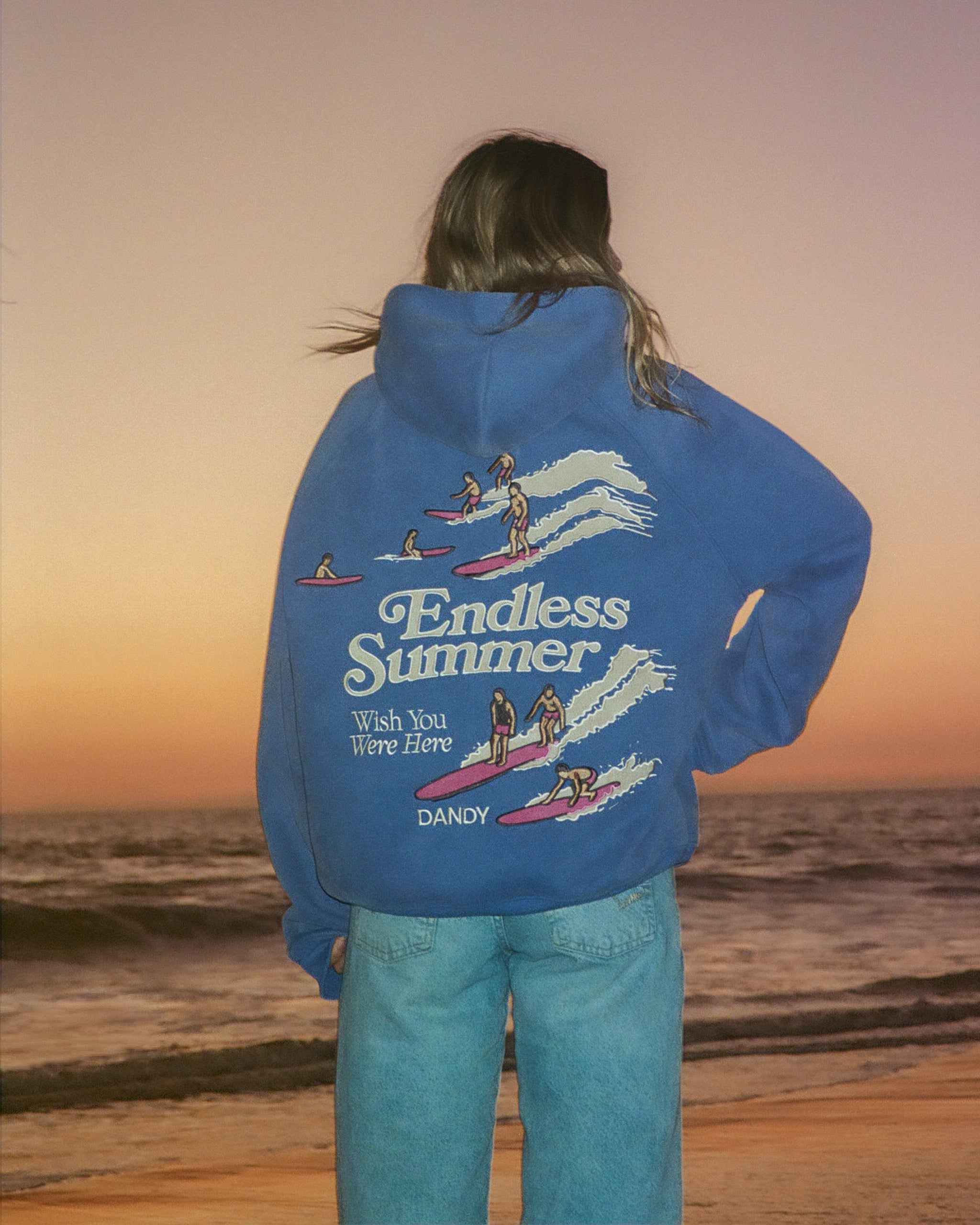 "Endless Summer" Oversized Lux Hoodie in Vintage Washed Blue standing on the beach at sunset